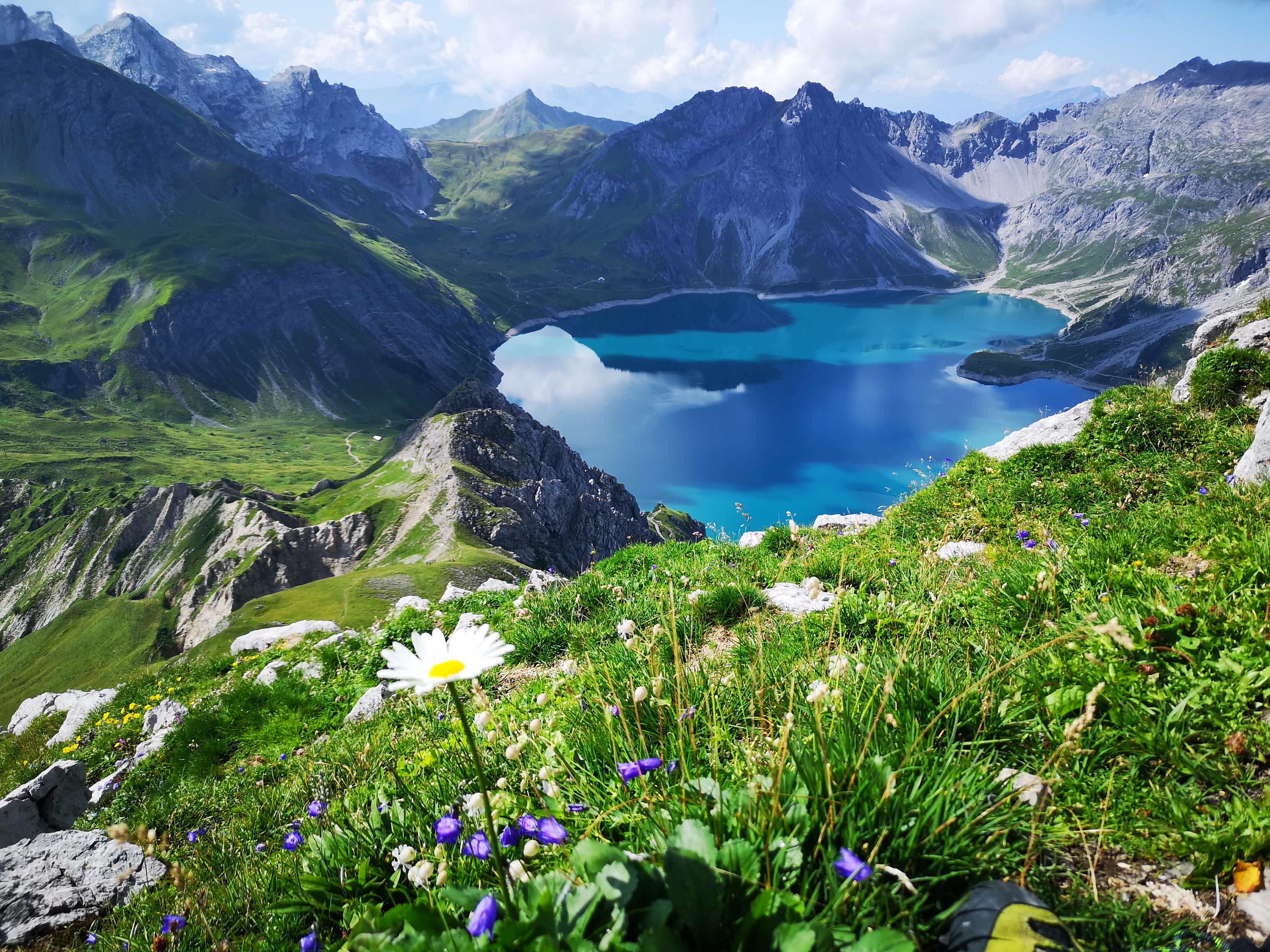Turquoise mountain lake surrounded by rocky peaks and green fields HD Wallpaper