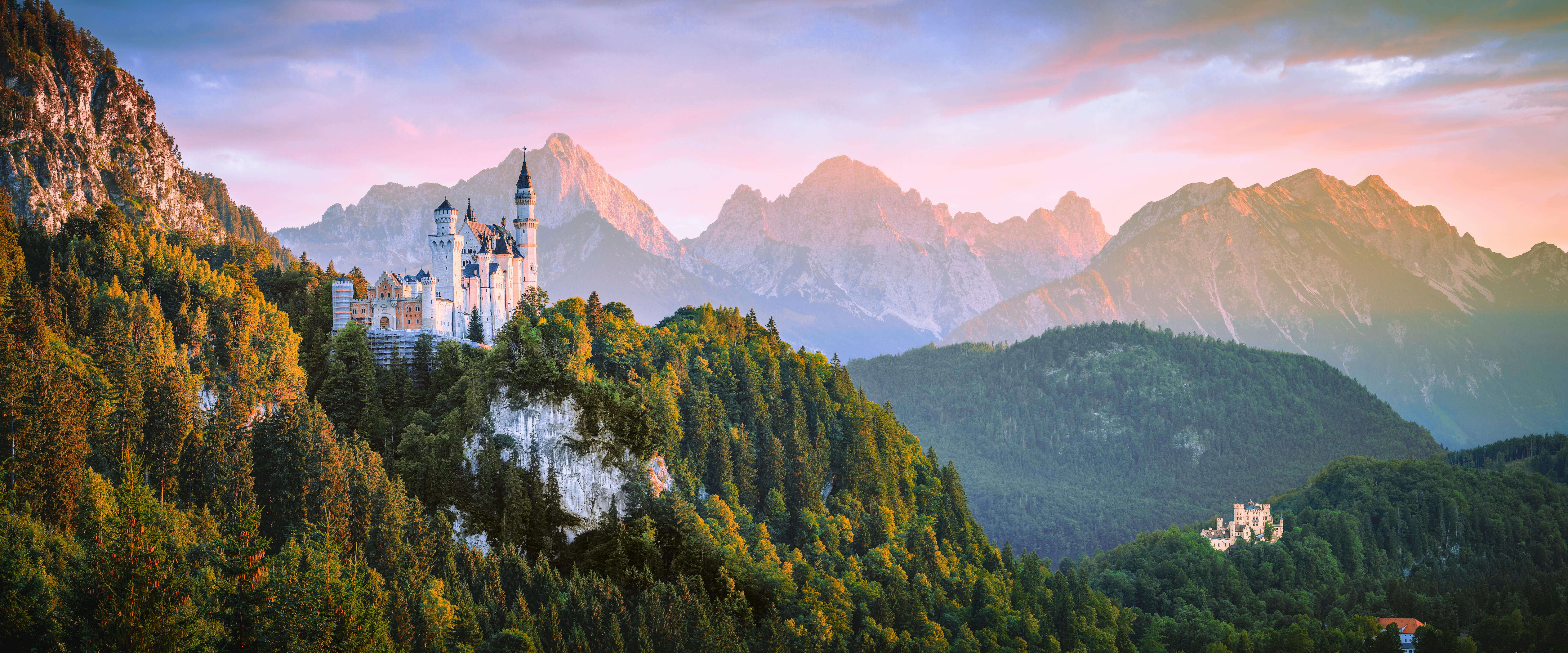 Neuschwanstein Castle on a forested hill with mountains HD Wallpaper