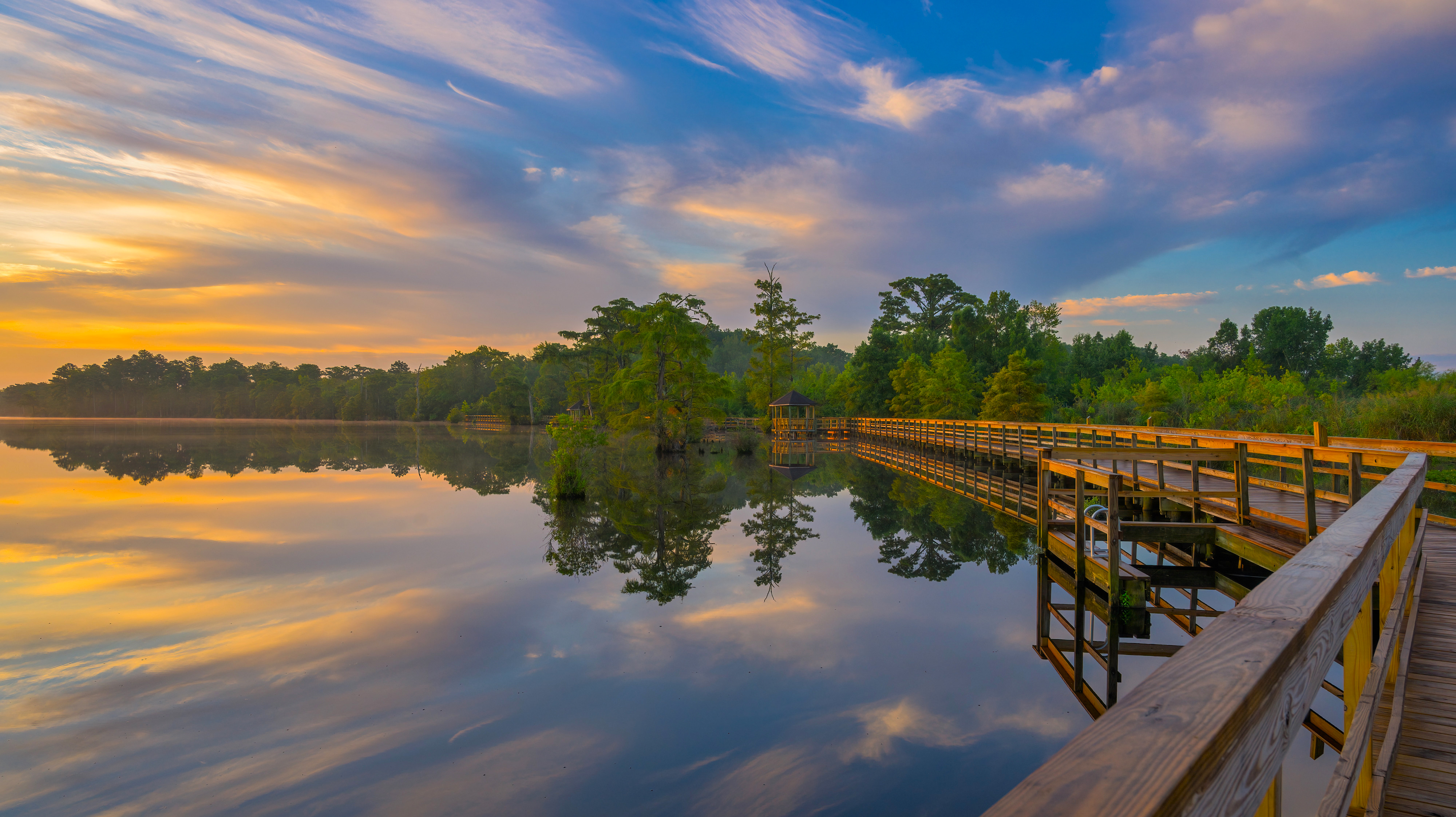 Wooden boardwalk over a calm lake at sunrise HD Wallpaper