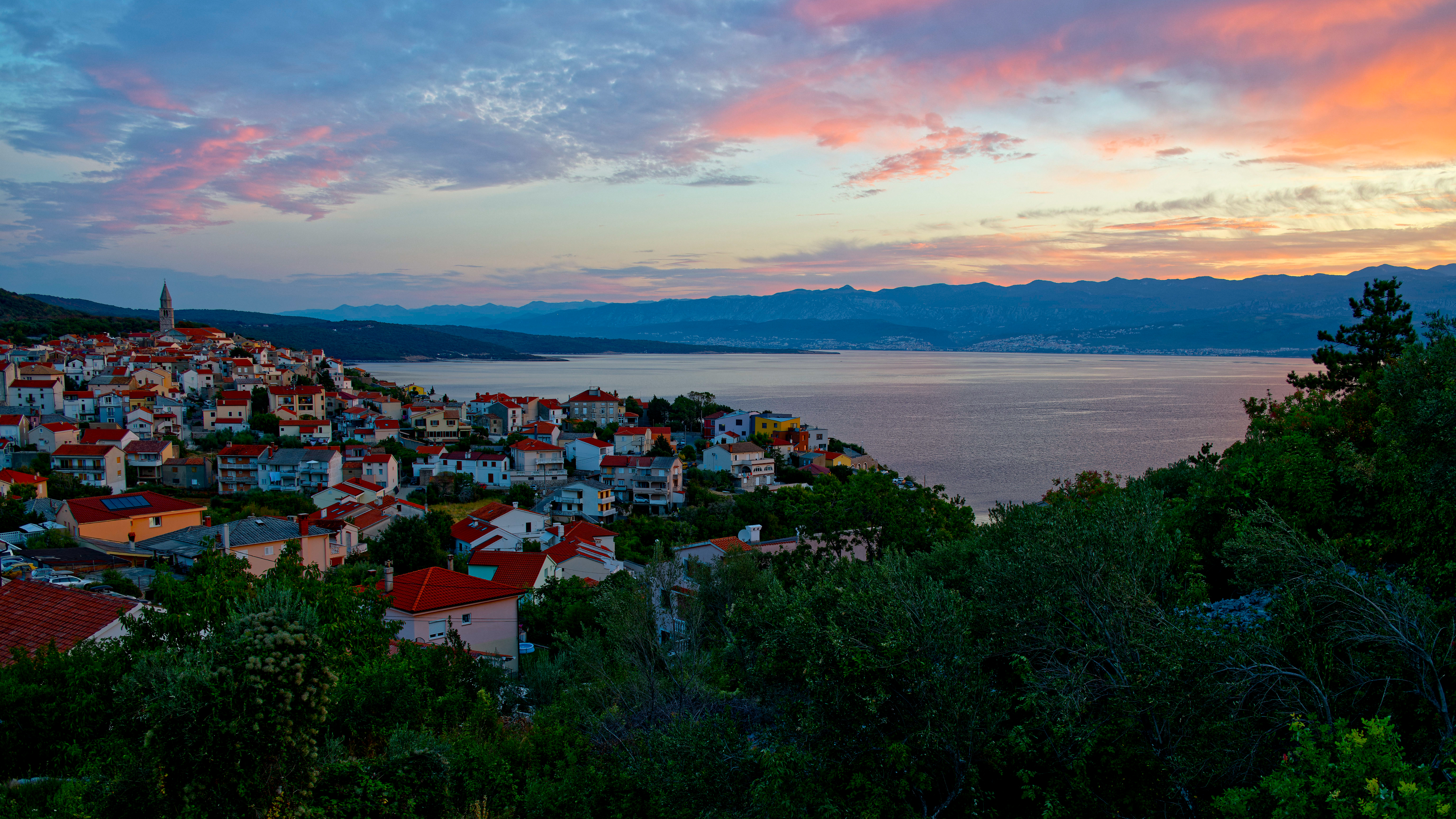 Coastal town at sunset with mountains in the background HD Wallpaper
