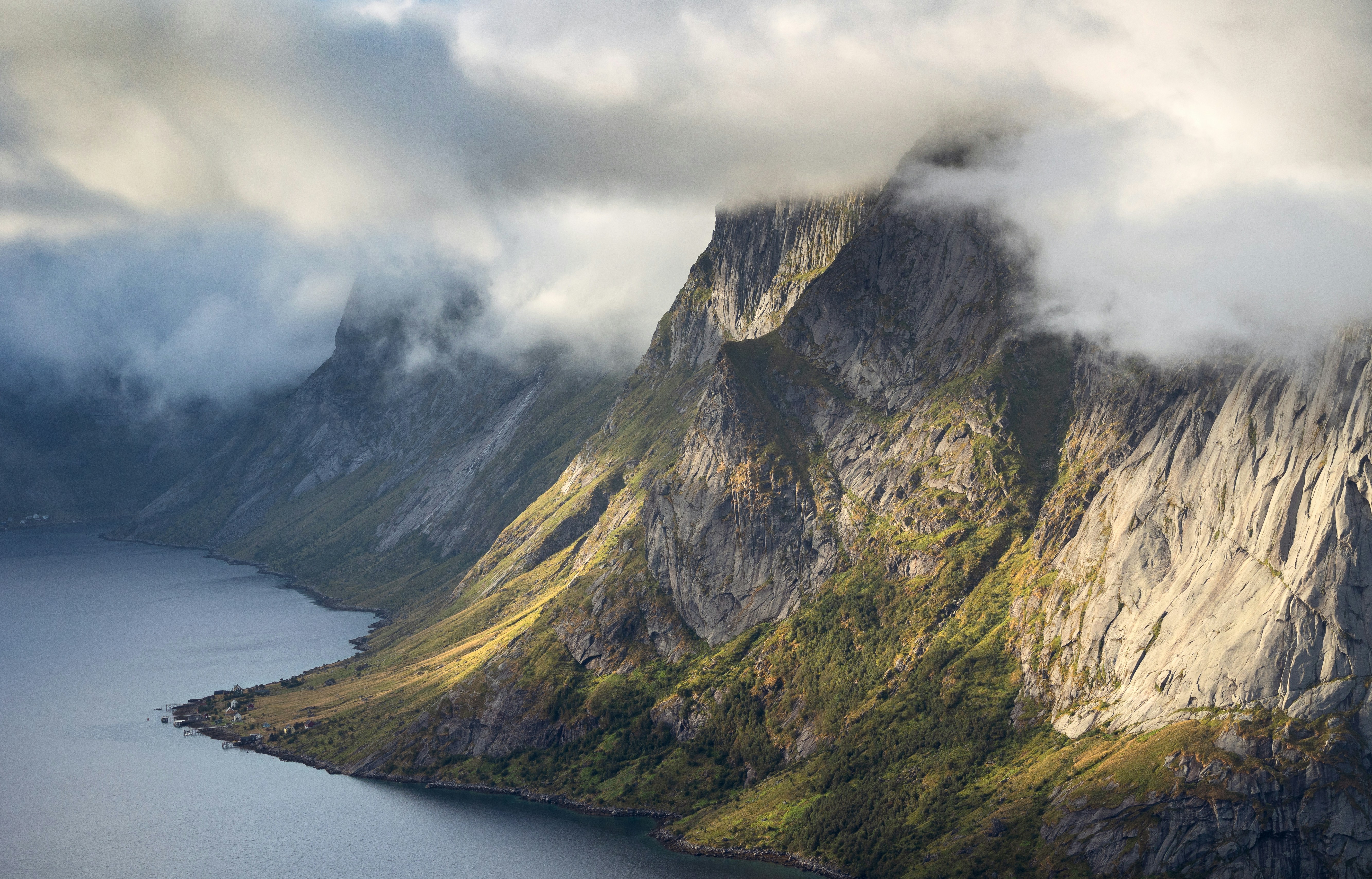 Mountains shrouded in clouds over a calm body of water HD Wallpaper
