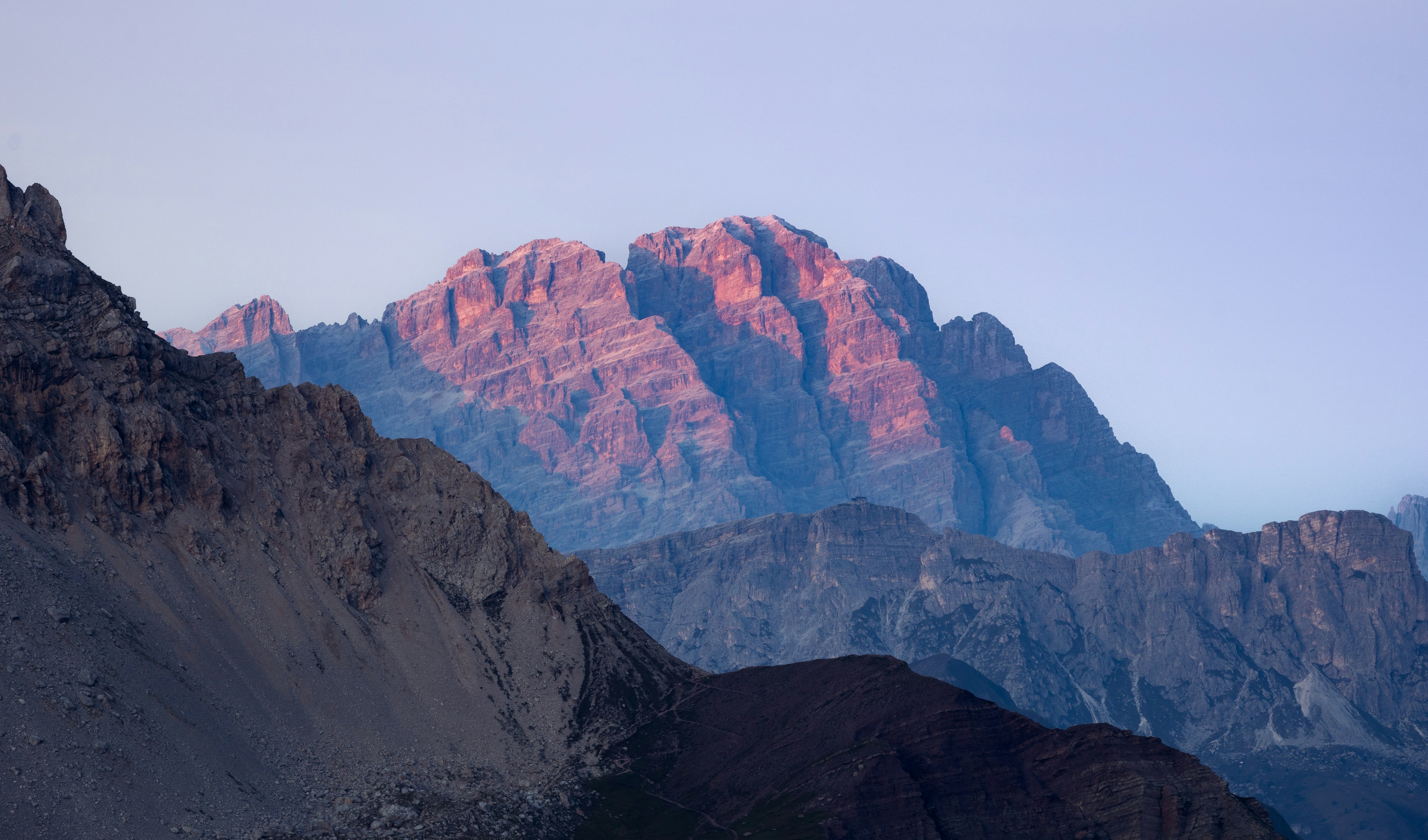 Sunlight illuminates rugged mountain peaks at dawn HD Wallpaper