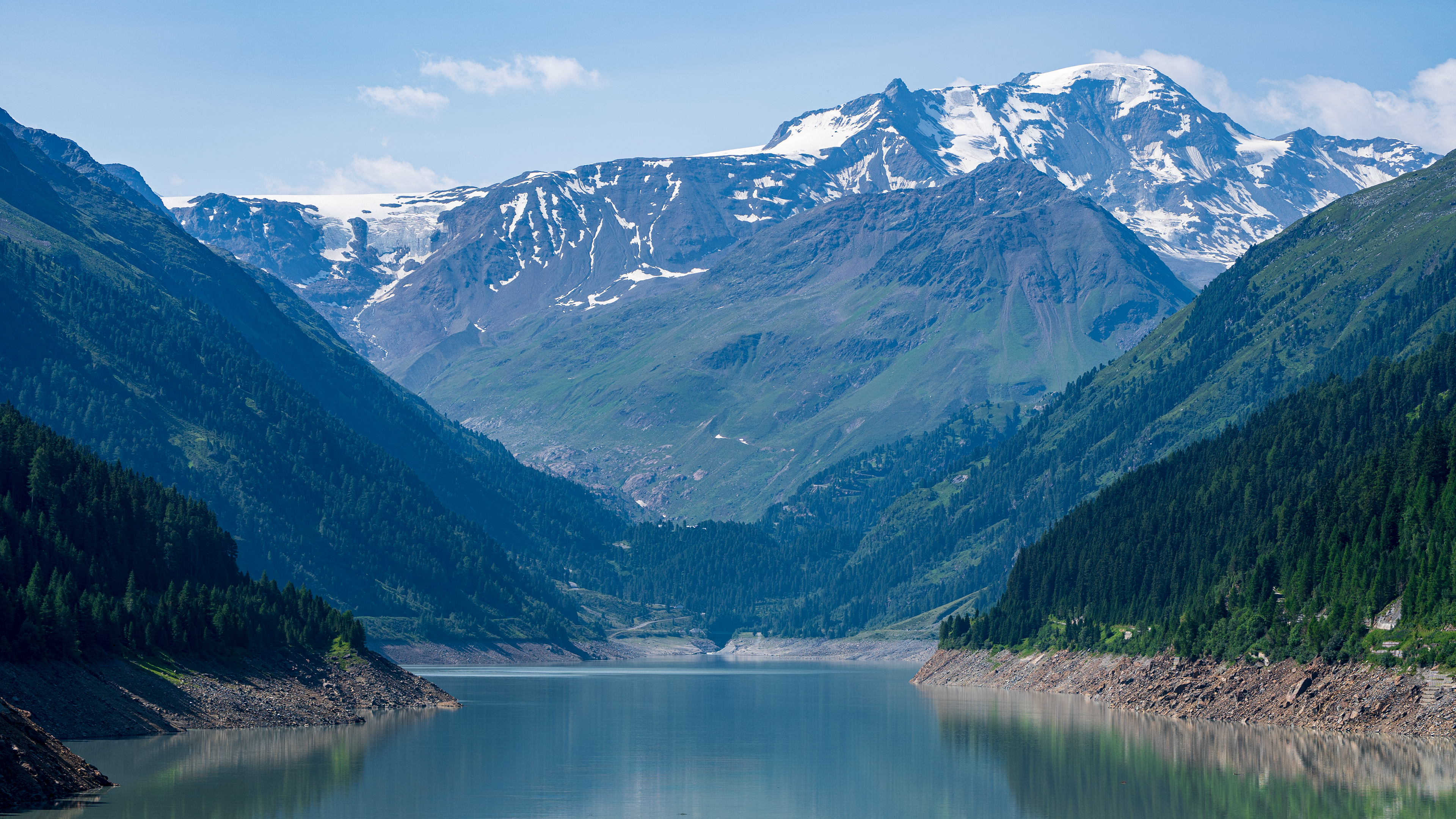 Snow-capped mountains reflected in a lake surrounded by forests HD Wallpaper