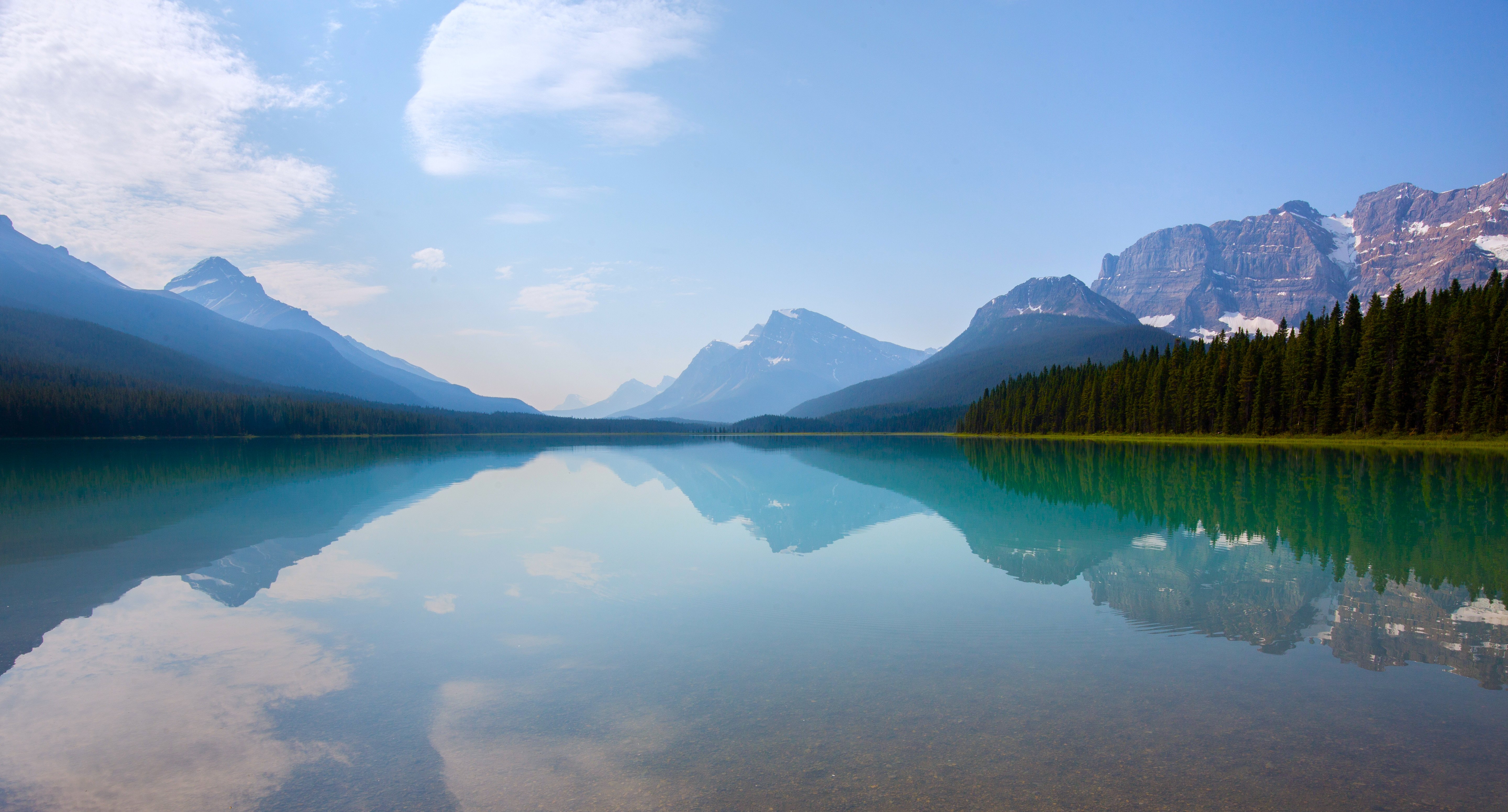 Calm lake reflecting mountains and forest under a blue sky HD Wallpaper