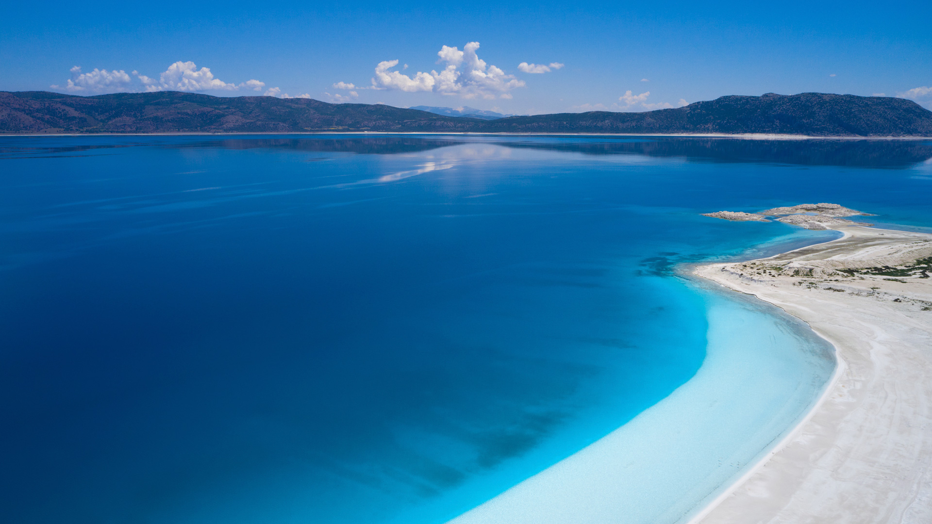 Blue lake with white sandy shore and mountains HD Wallpaper