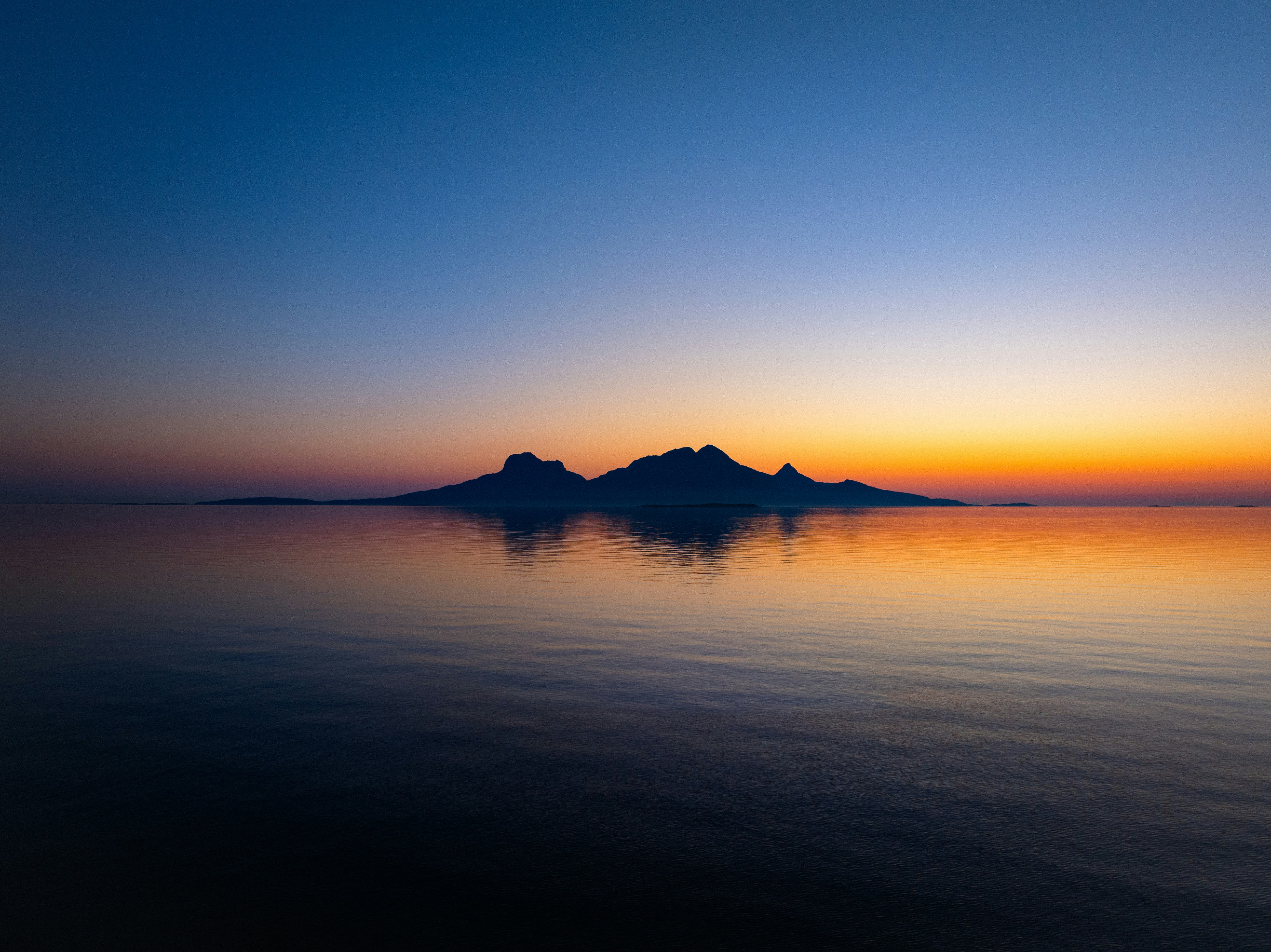 Island silhouette reflected in calm water at sunset HD Wallpaper
