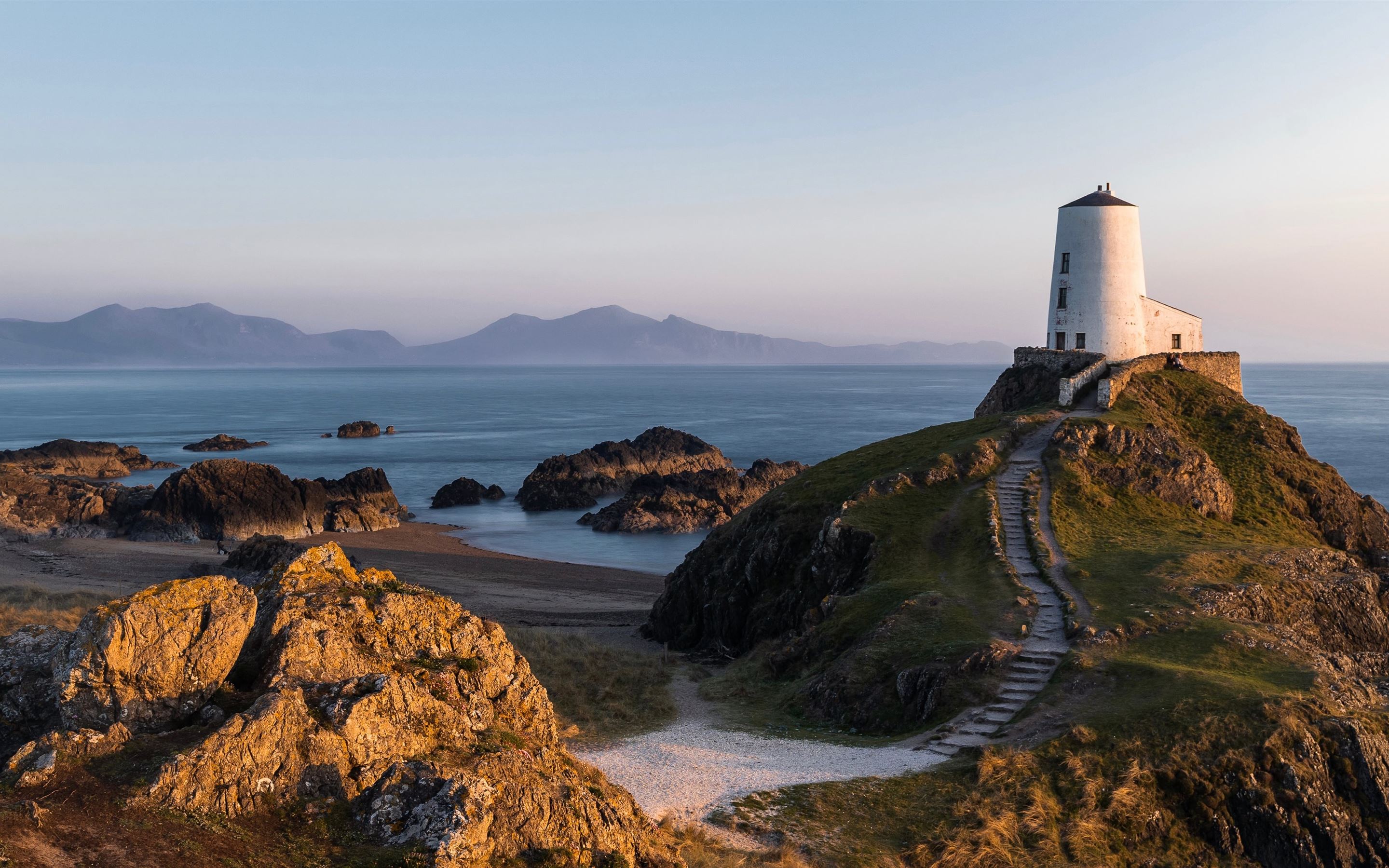 White lighthouse on a rocky island coast with hills in background HD Wallpaper