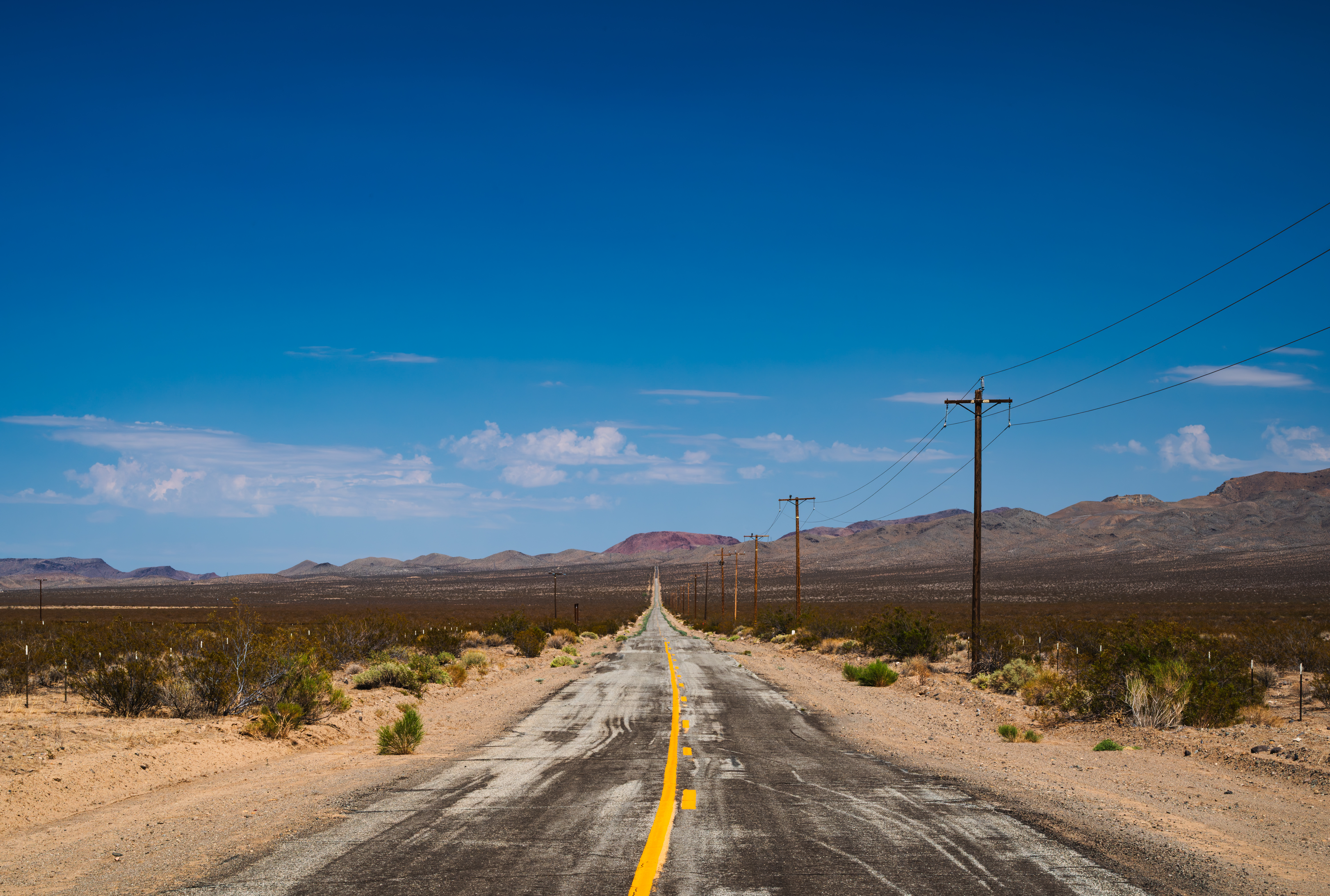 Desert highway with utility poles and mountains HD Wallpaper