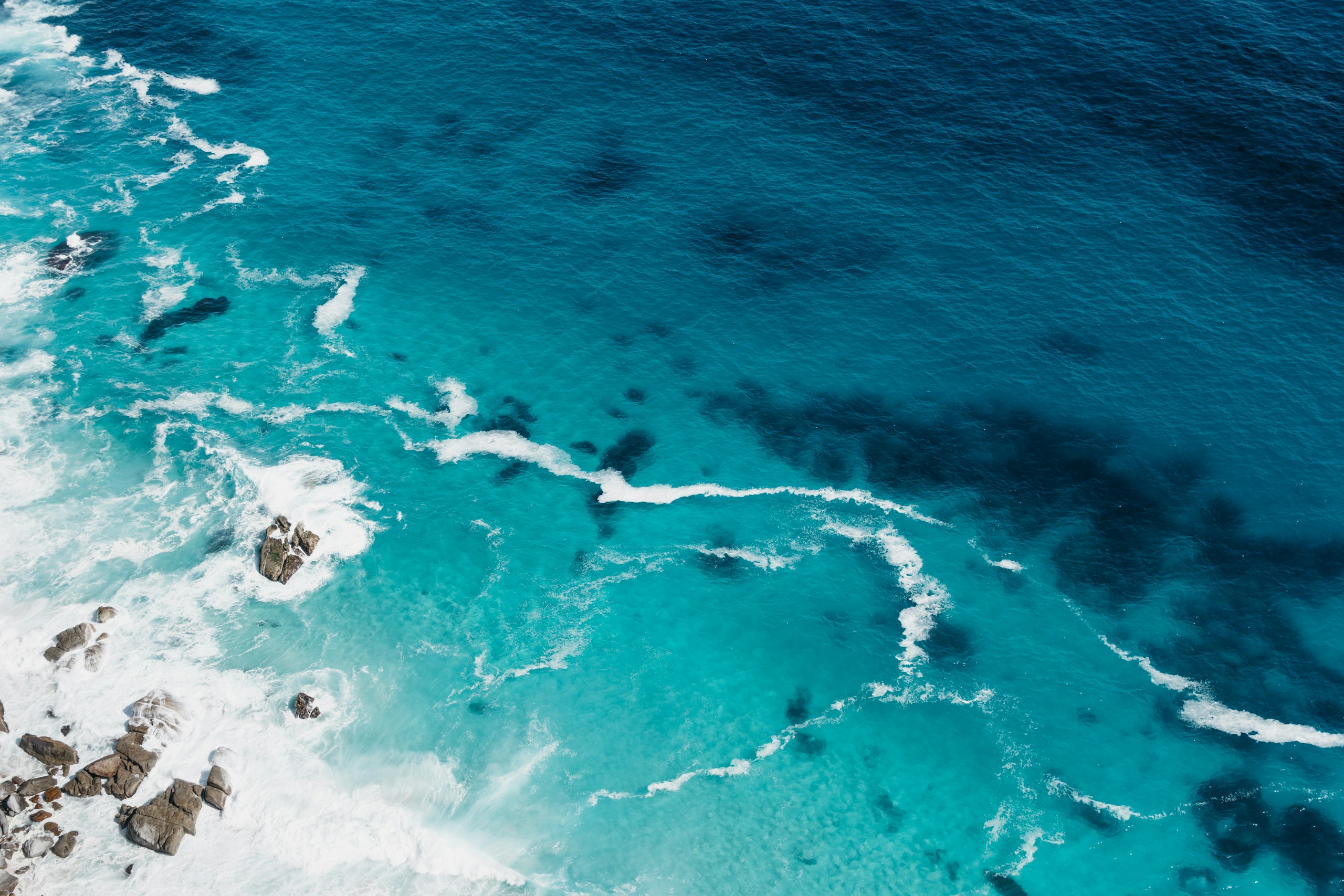 Aerial view of turquoise ocean water and rocky shore HD Wallpaper