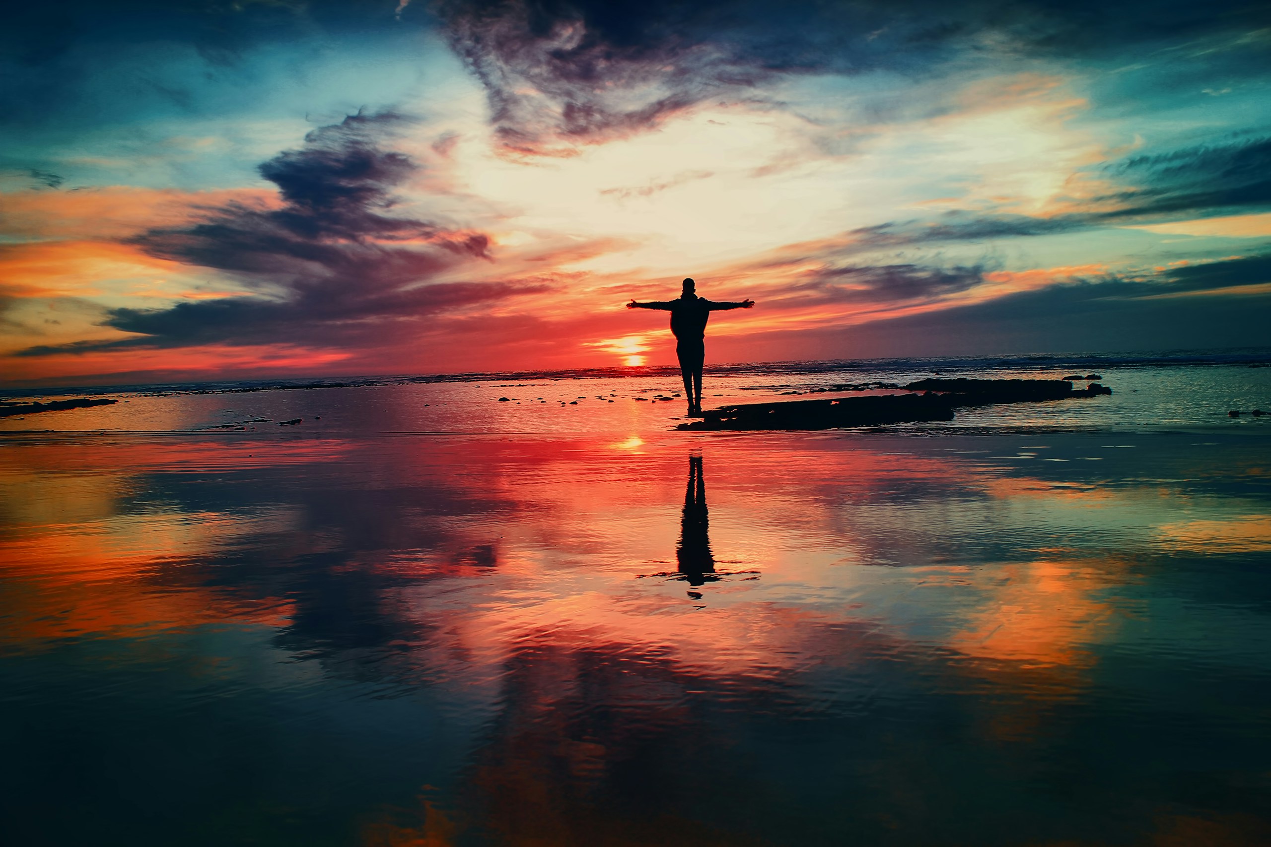 Silhouette of a person standing on a beach at sunset HD Wallpaper