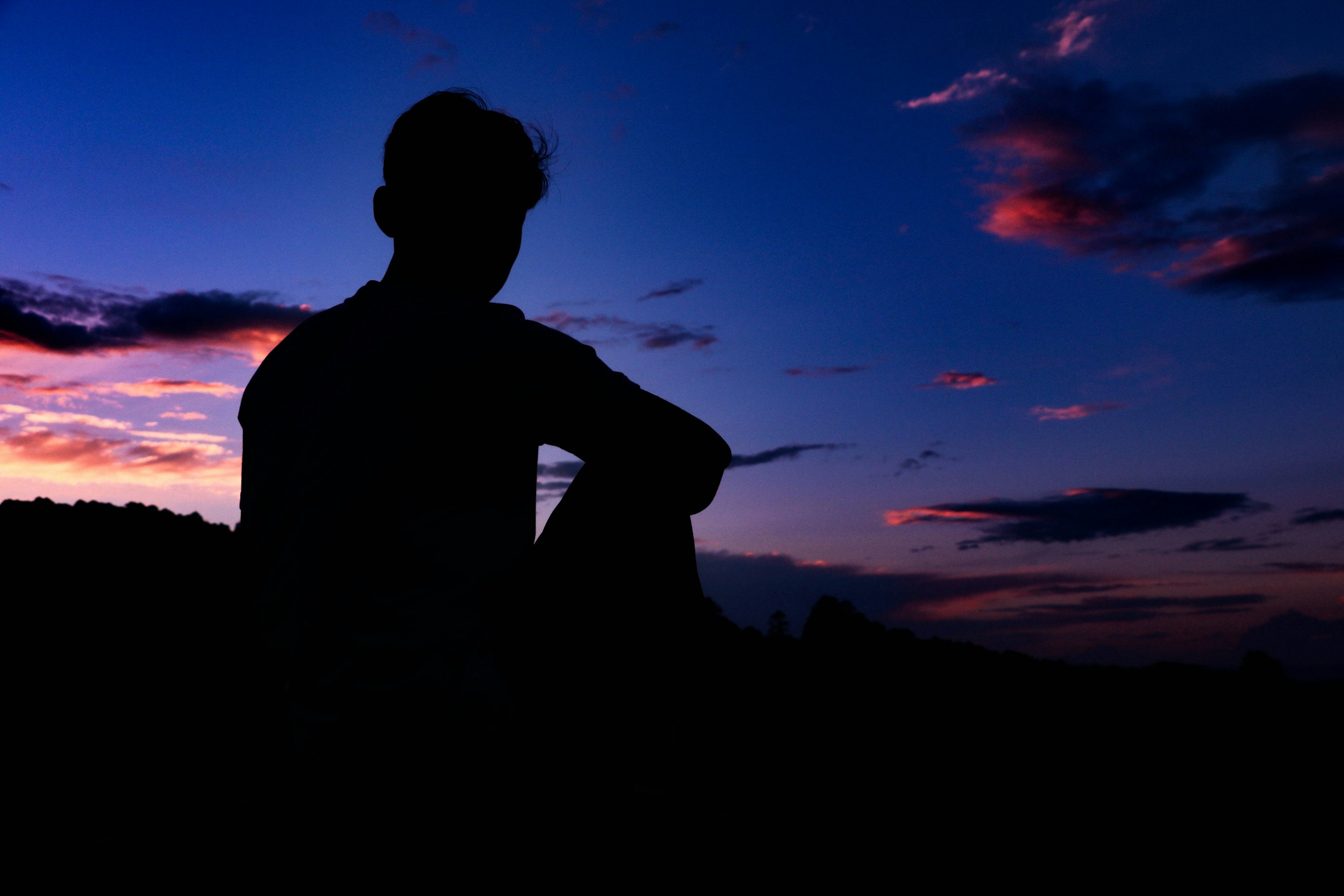 Silhouette of a man sitting under a twilight sky HD Wallpaper