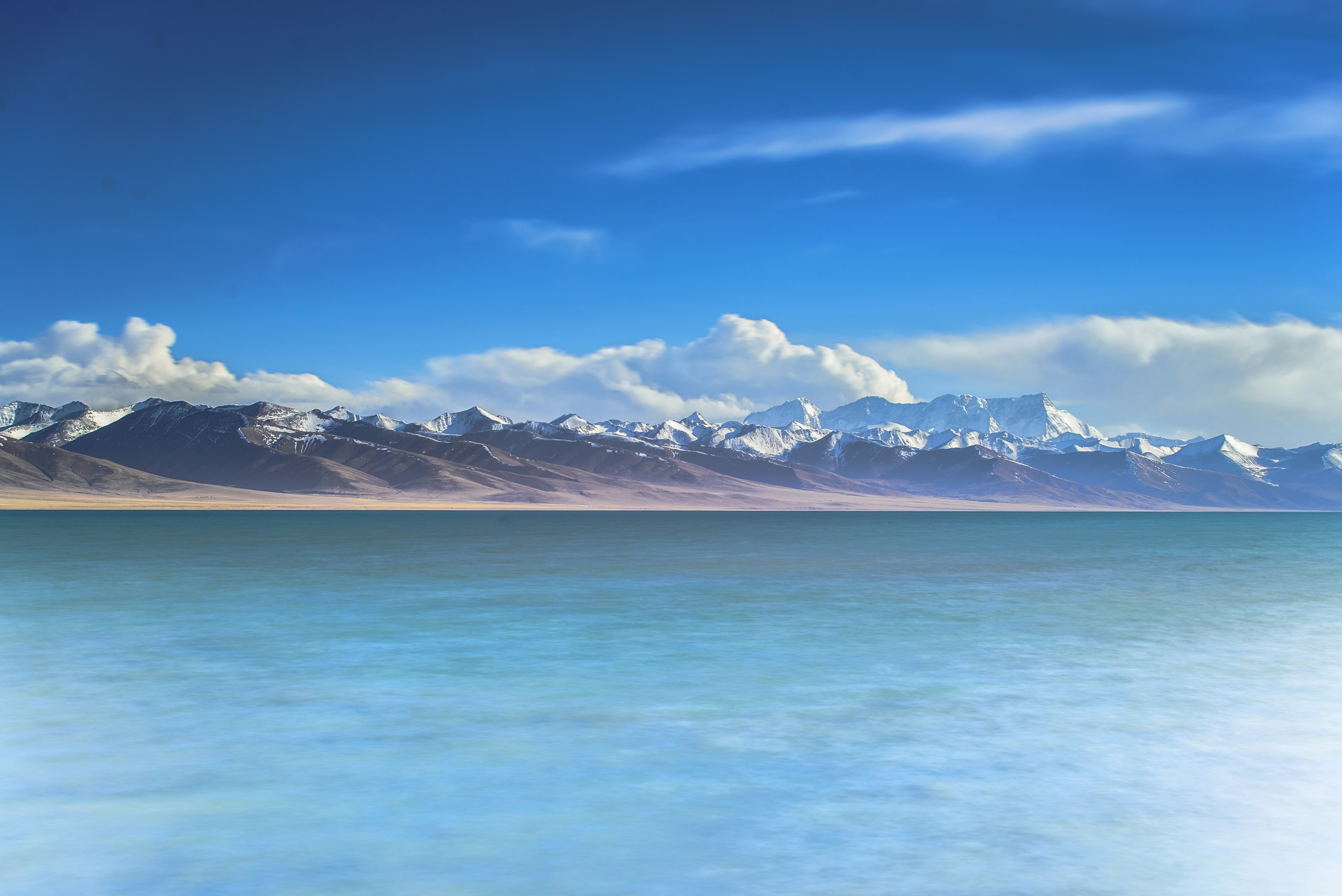 Snowy mountain range behind a calm blue lake HD Wallpaper