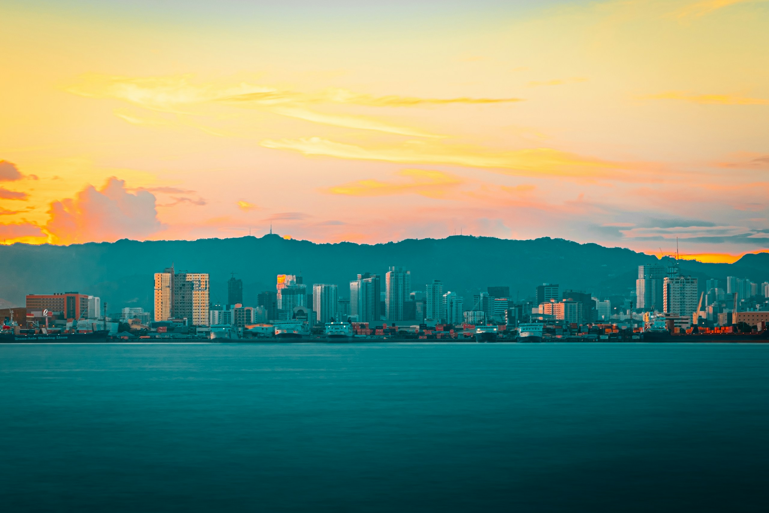 City skyline across body of water during sunset HD Wallpaper