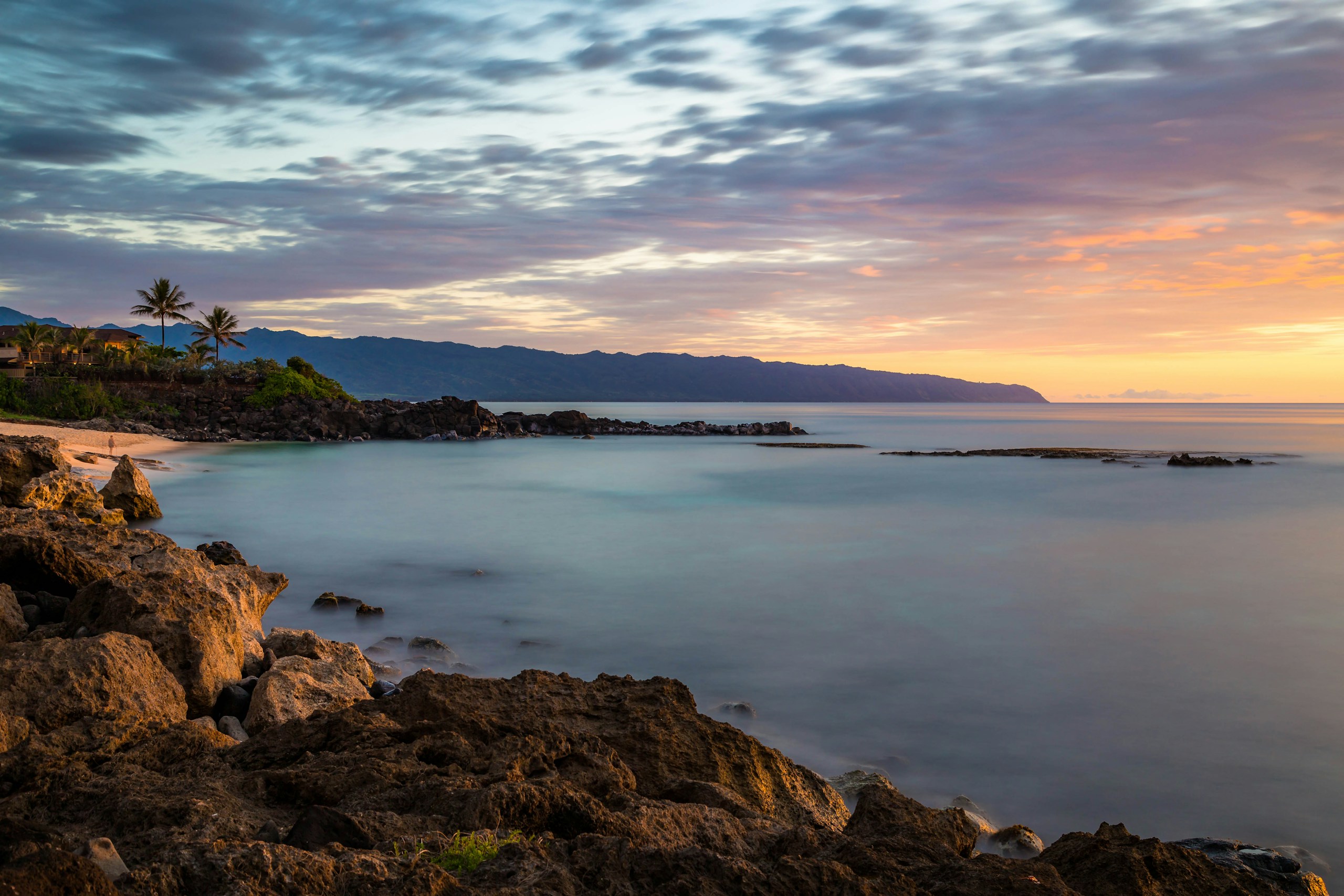 Rocky shoreline at sunset with distant mountains HD Wallpaper
