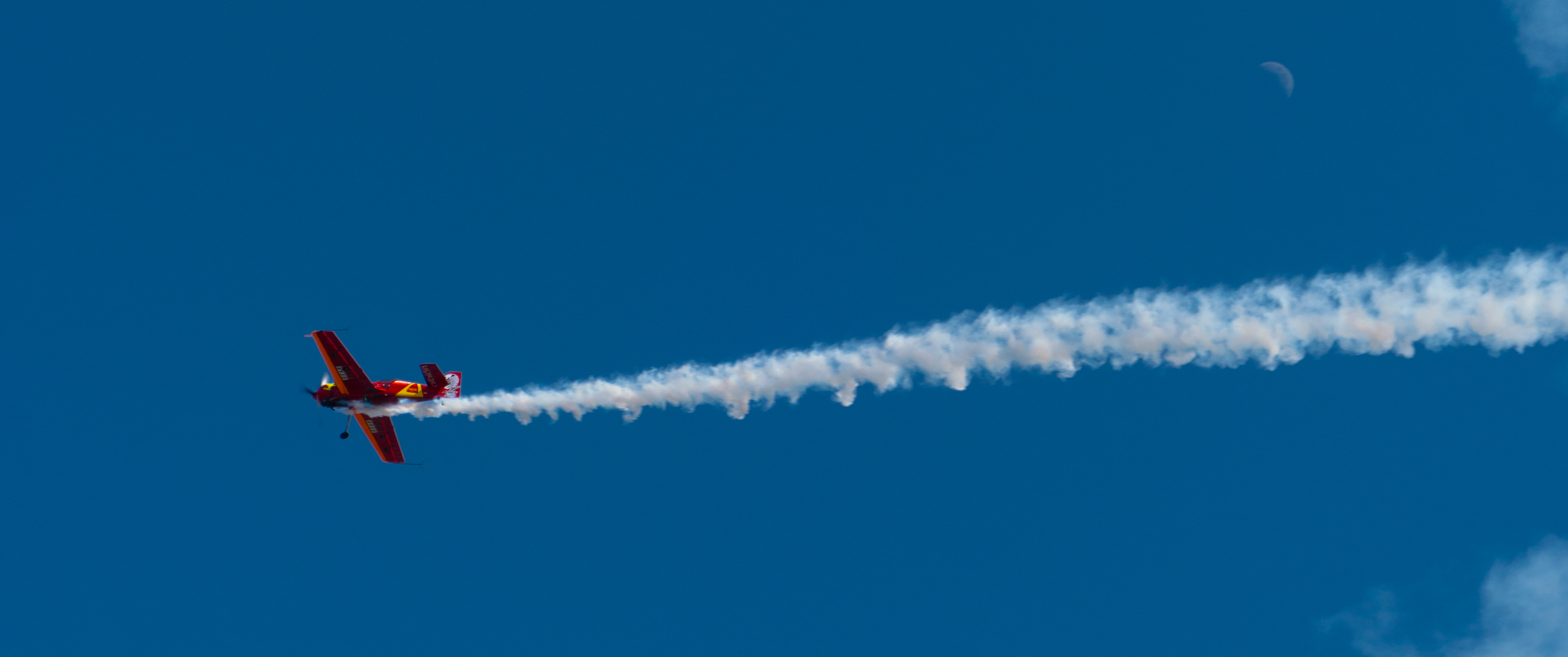 Red stunt plane flying in blue sky with smoke trail HD Wallpaper