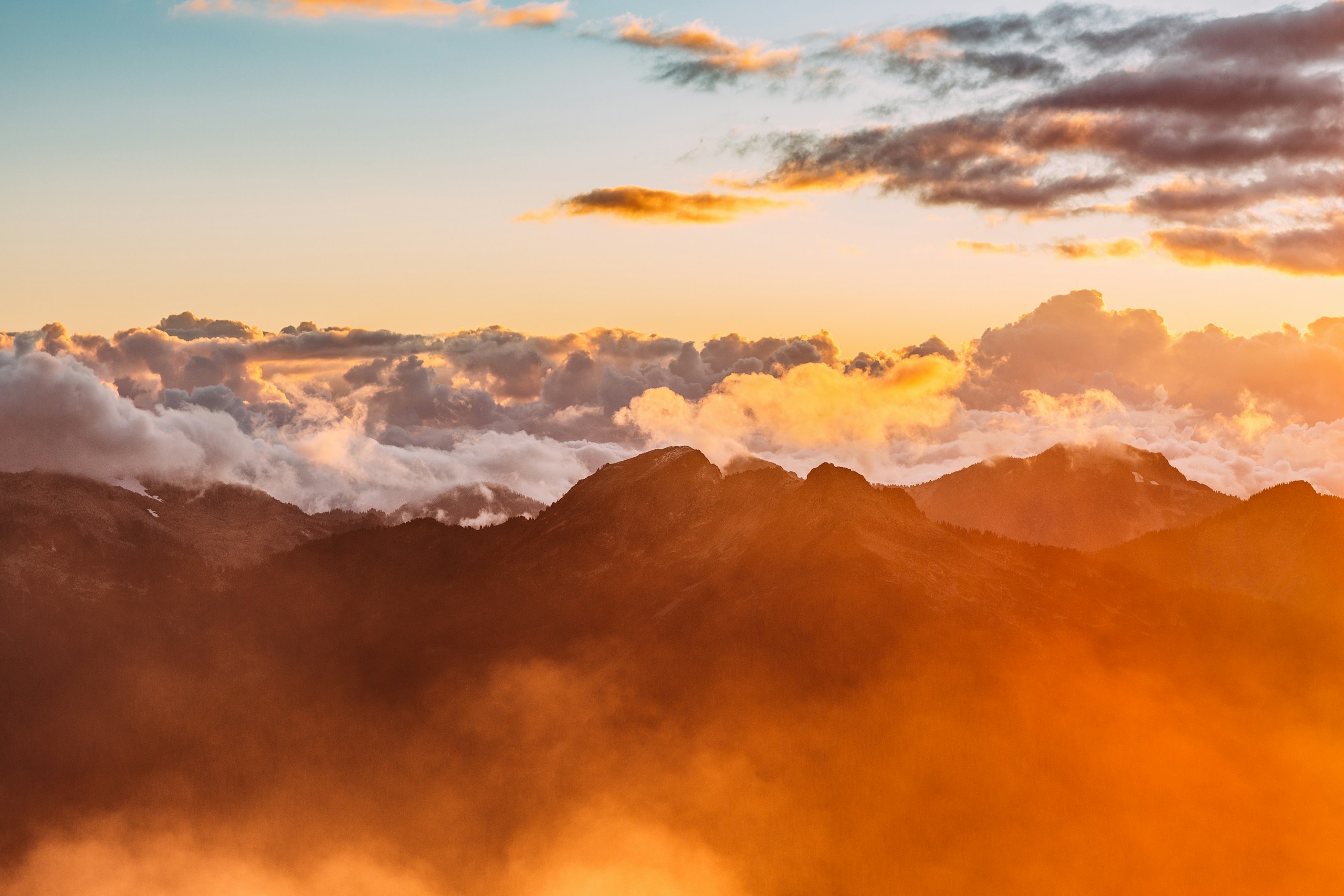 Mountain peaks above orange clouds at golden hour HD Wallpaper