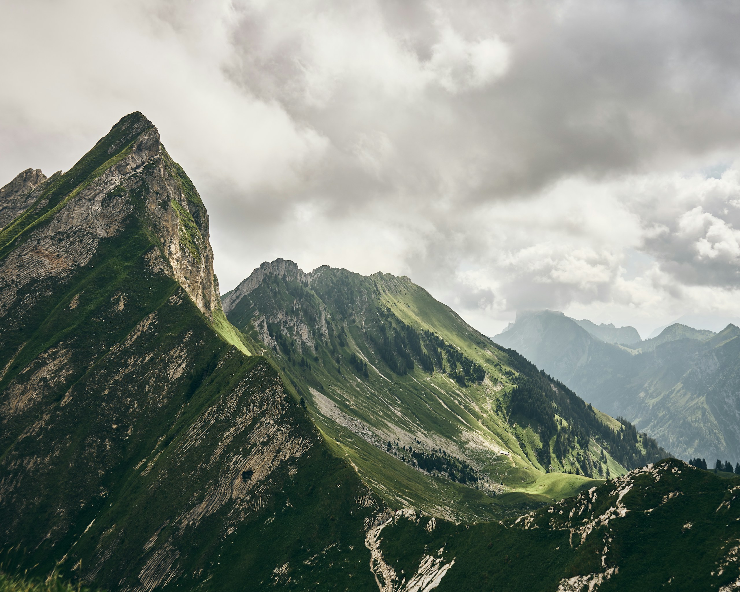 Green mountain peaks under a cloudy sky HD Wallpaper