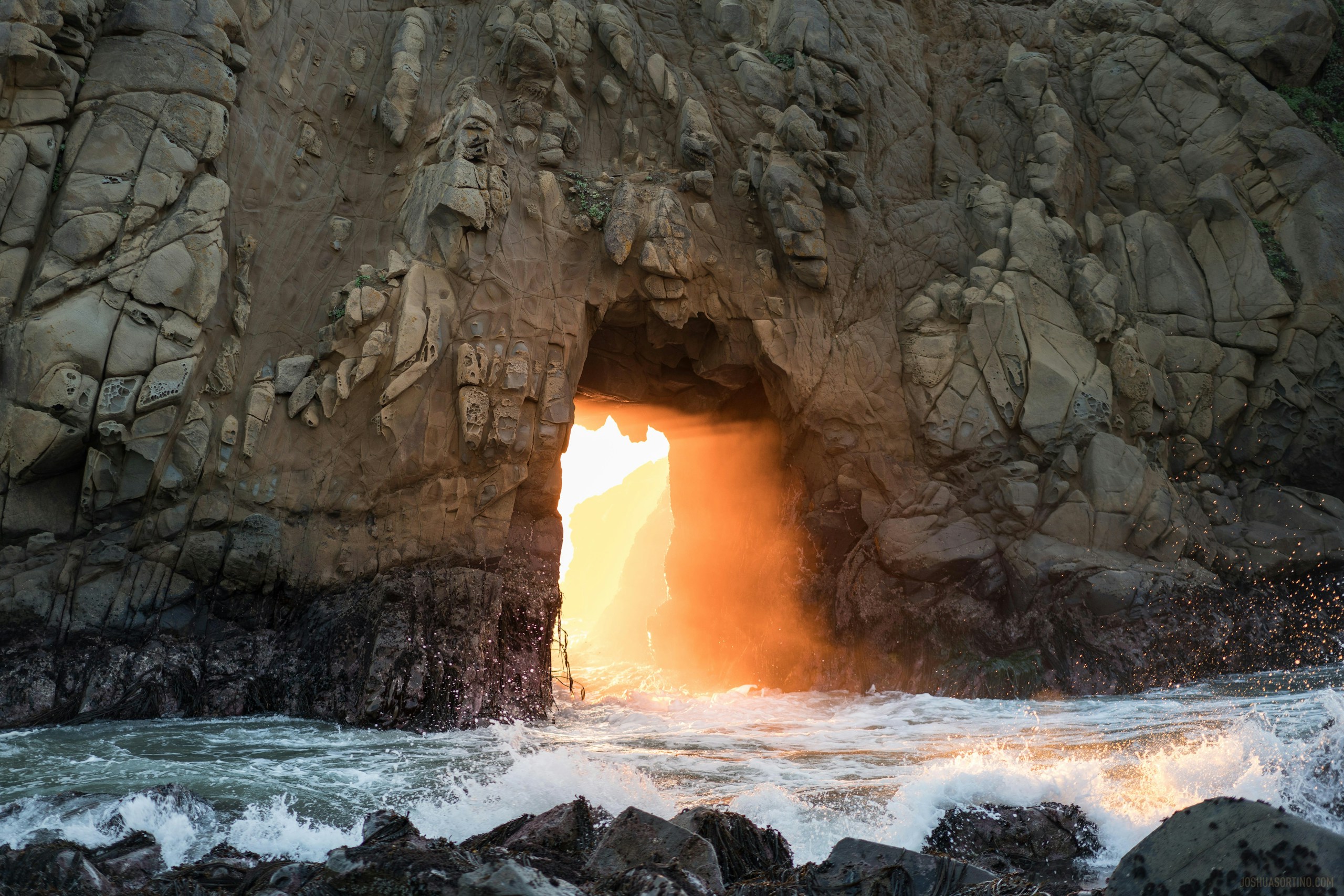 Golden light shining through a coastal rock arch HD Wallpaper