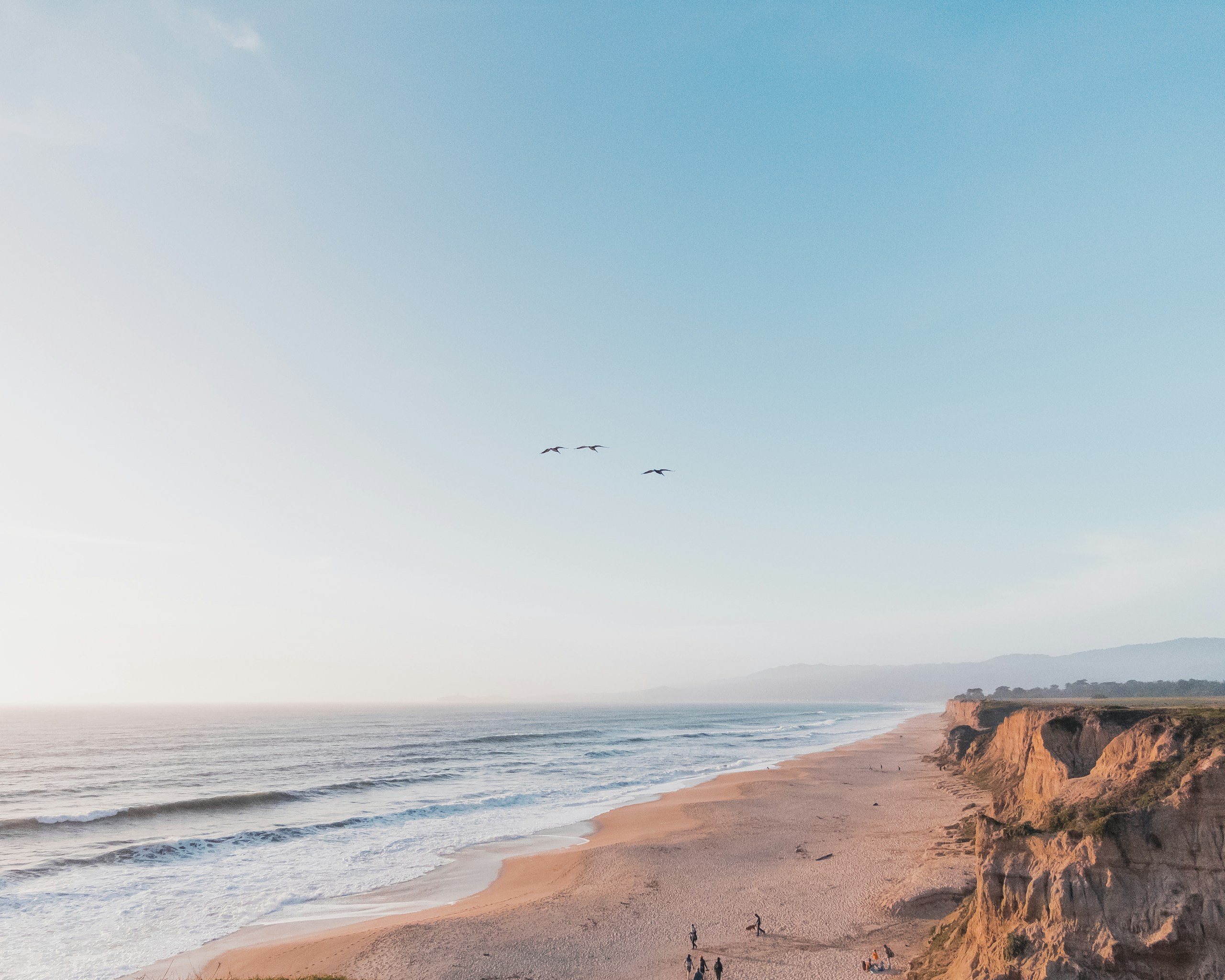 Coastal cliffs and sandy beach under a clear sky HD Wallpaper