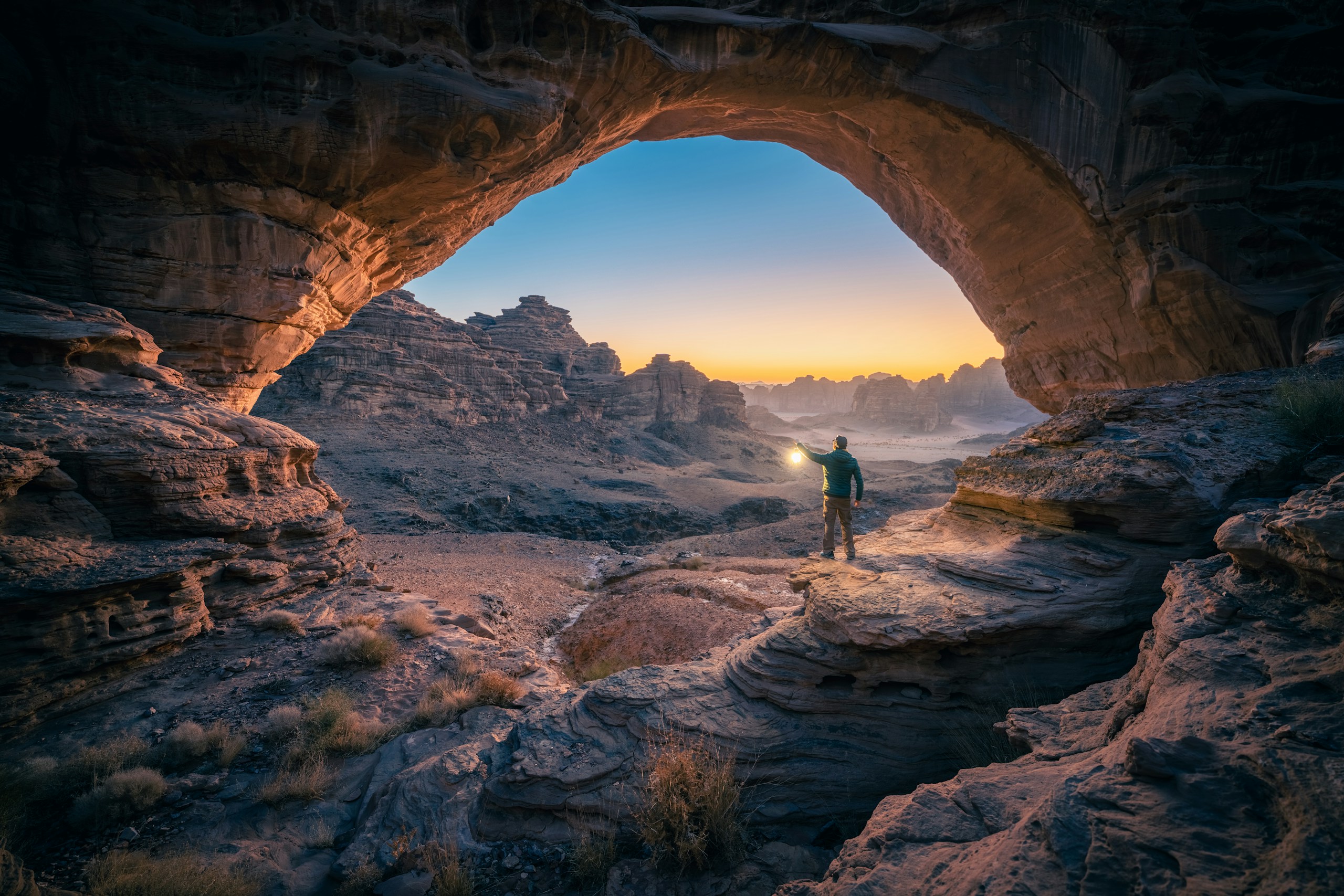 Man standing under natural rock arch at sunset HD Wallpaper