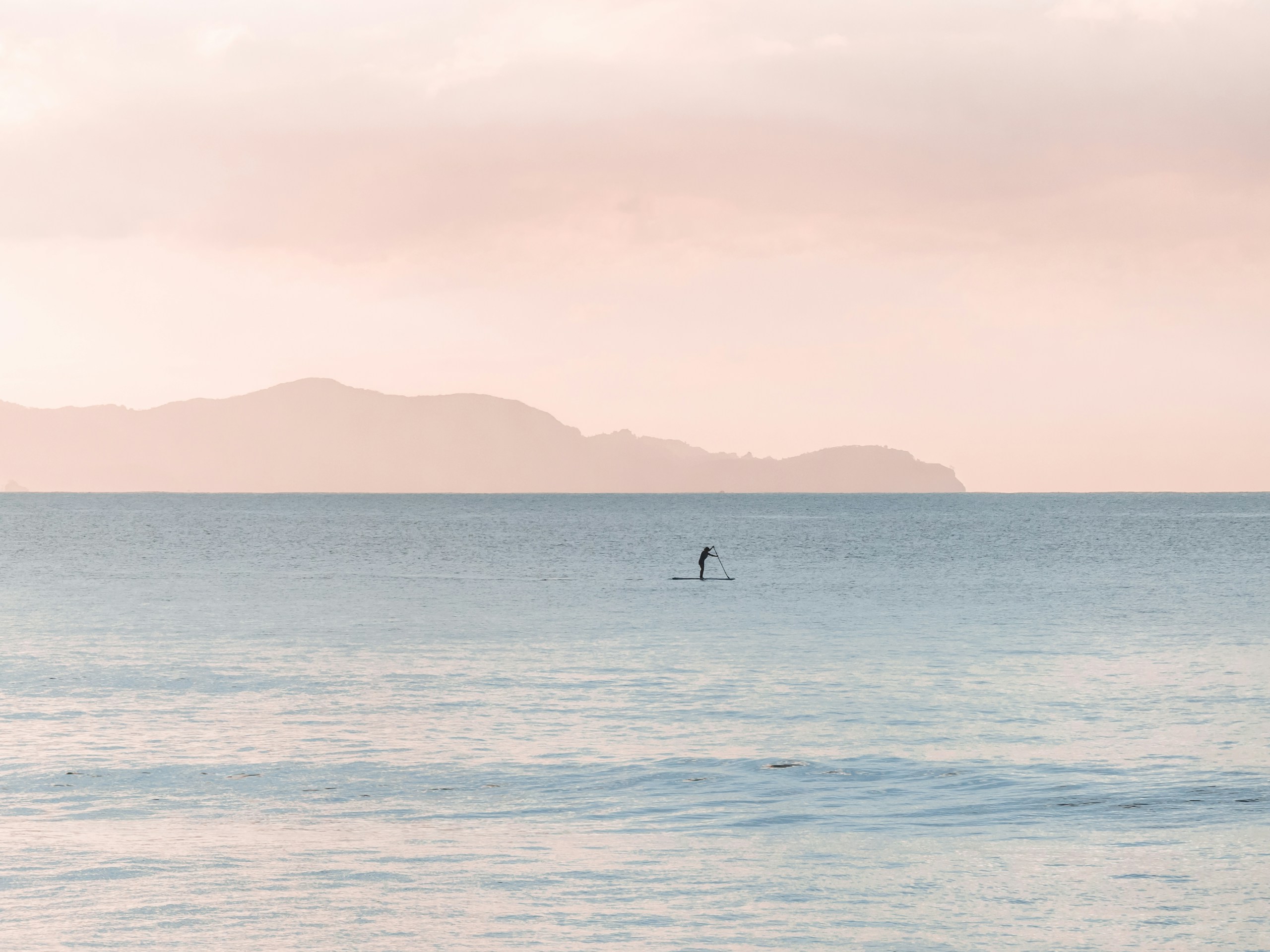 Person paddleboarding on calm sea under pastel sky HD Wallpaper