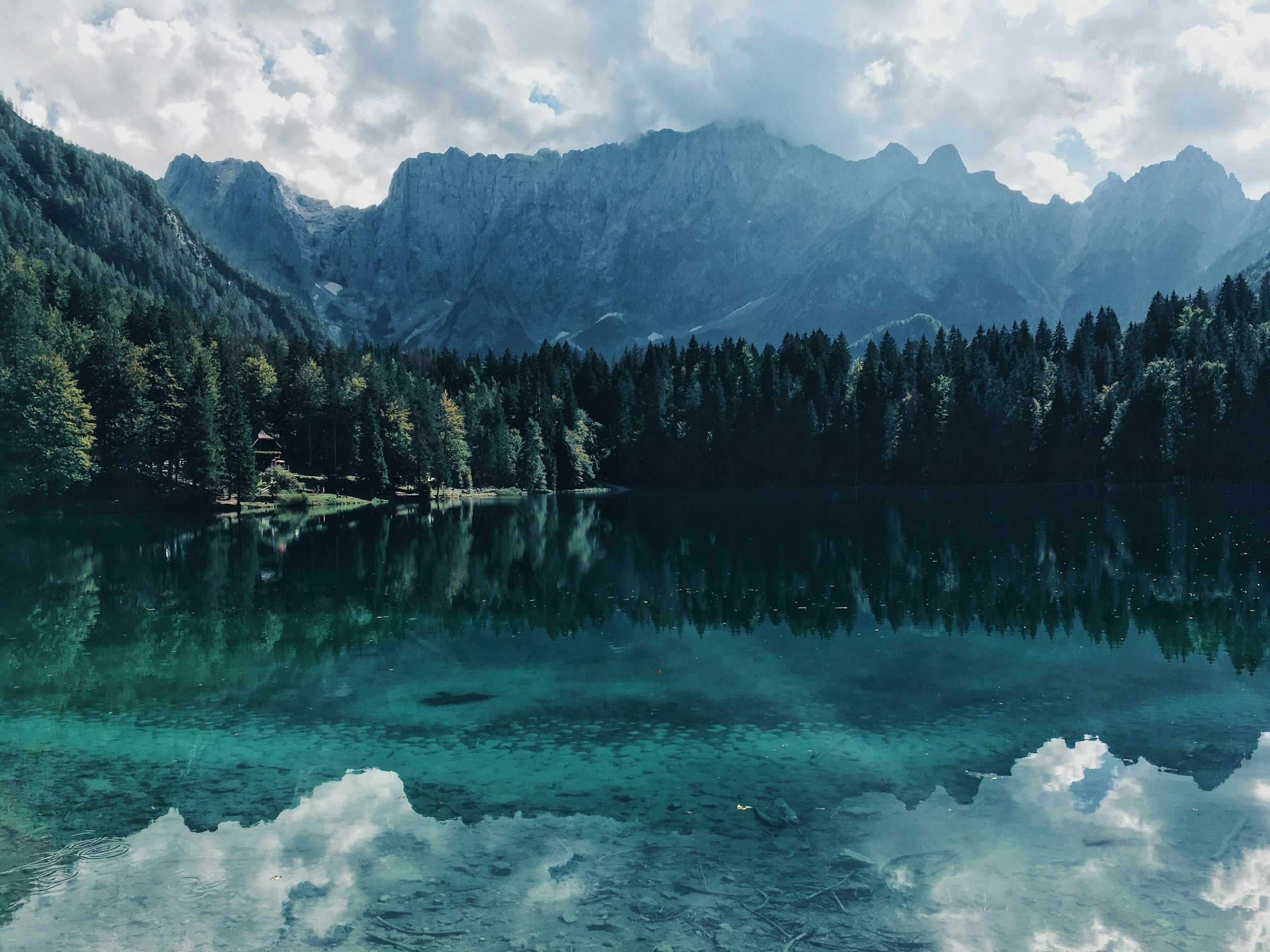 Clear turquoise alpine lake reflecting mountains and forest HD Wallpaper