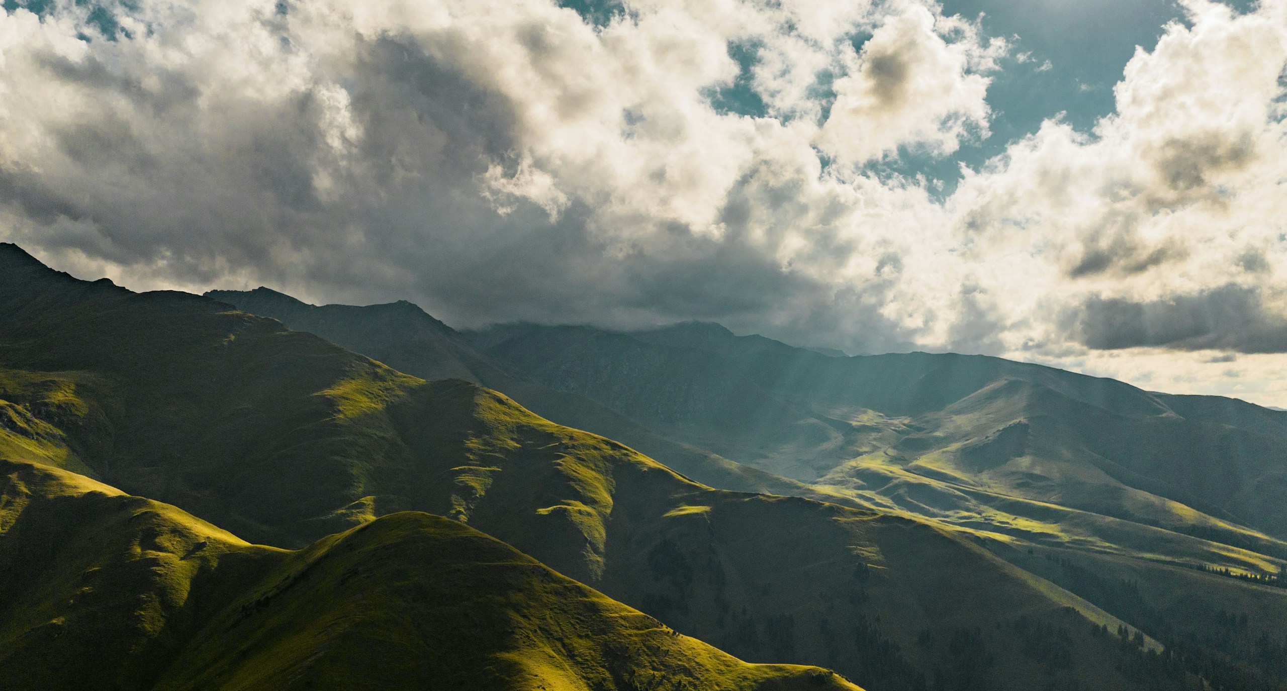 Green rolling hills under a cloudy sky with sunbeams HD Wallpaper