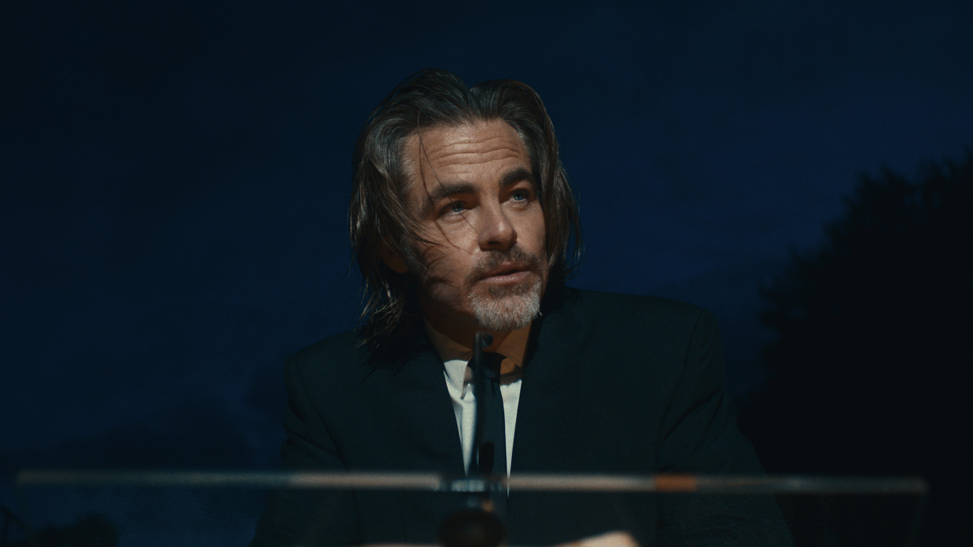 Chris Pine wearing a black suit at a podium HD Wallpaper