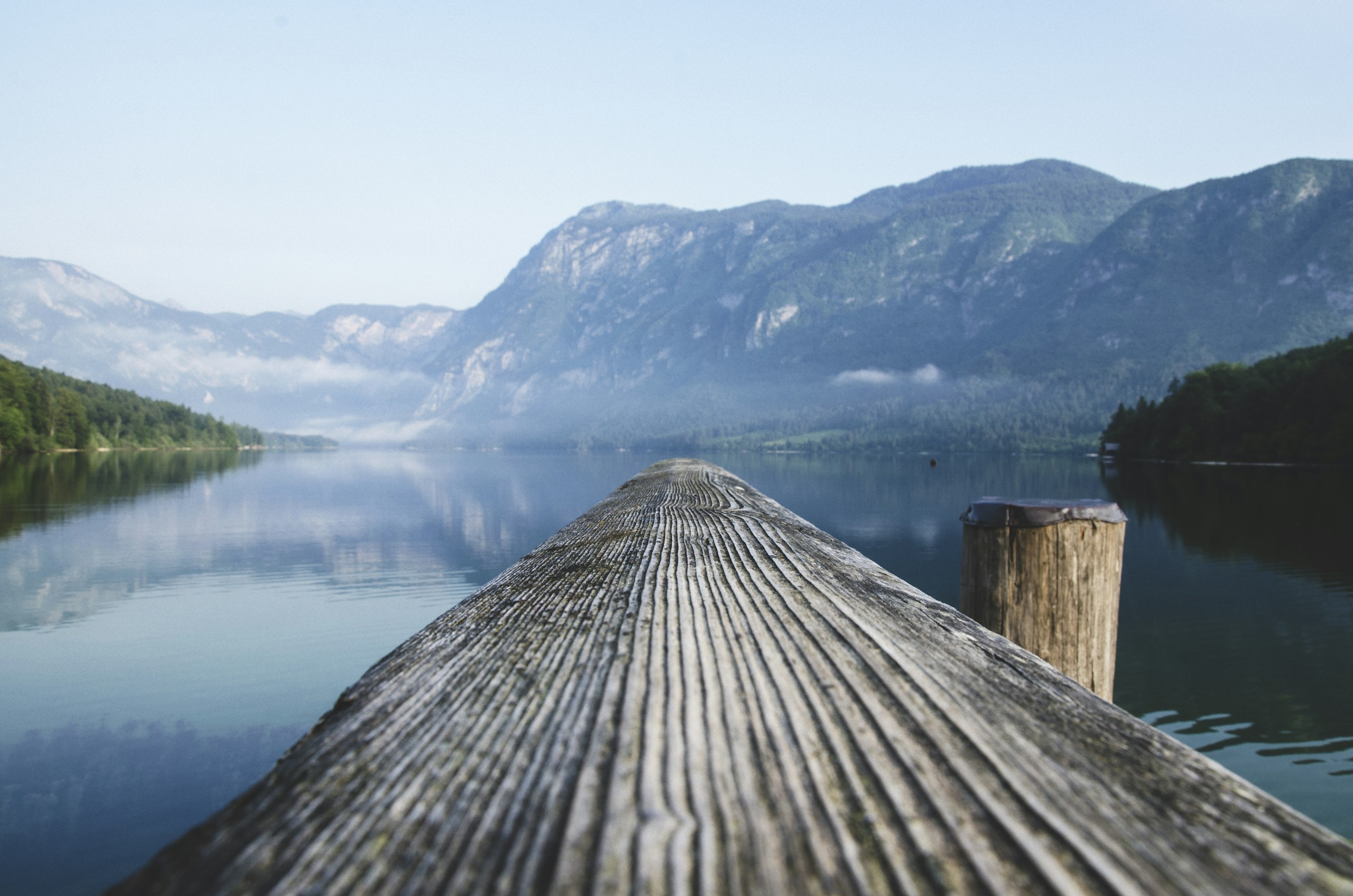 Wooden dock railing leading to a calm mountain lake HD Wallpaper