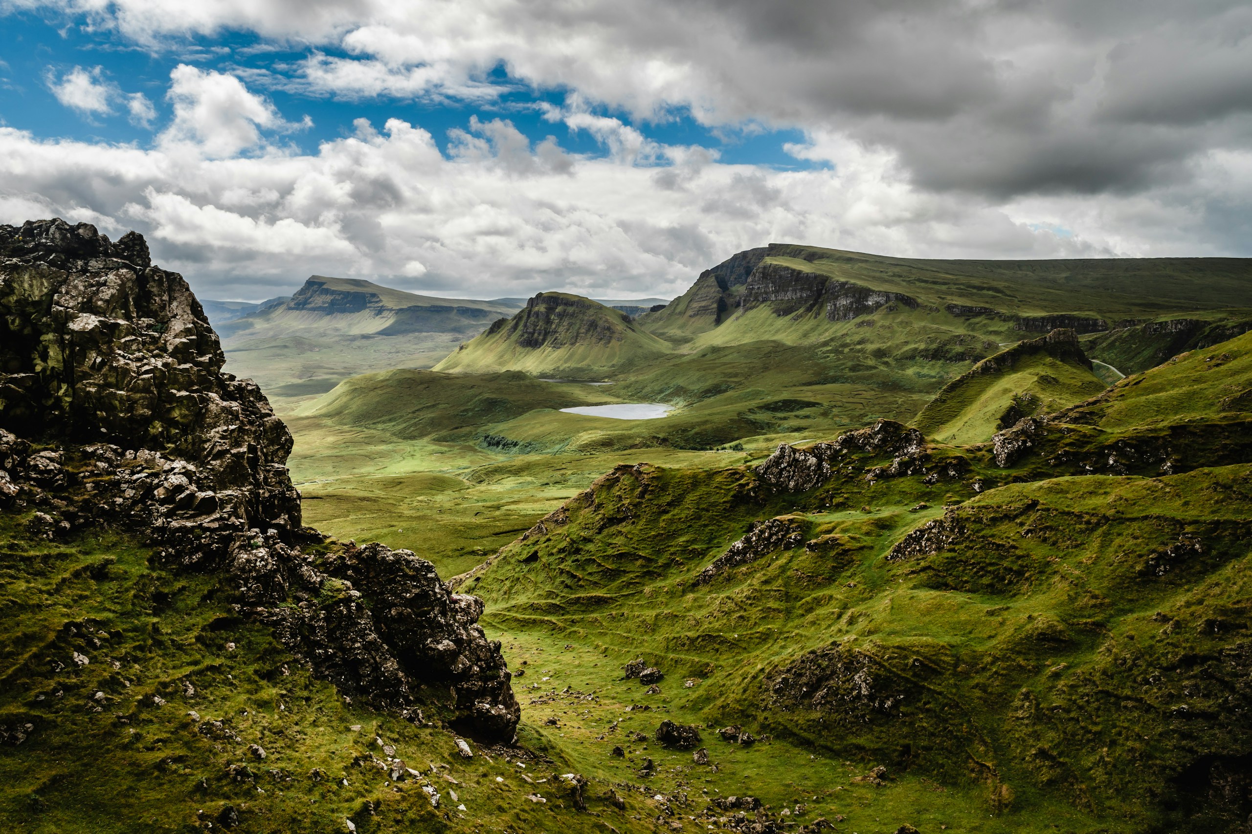 Green mountains and rocky cliffs under a cloudy sky HD Wallpaper