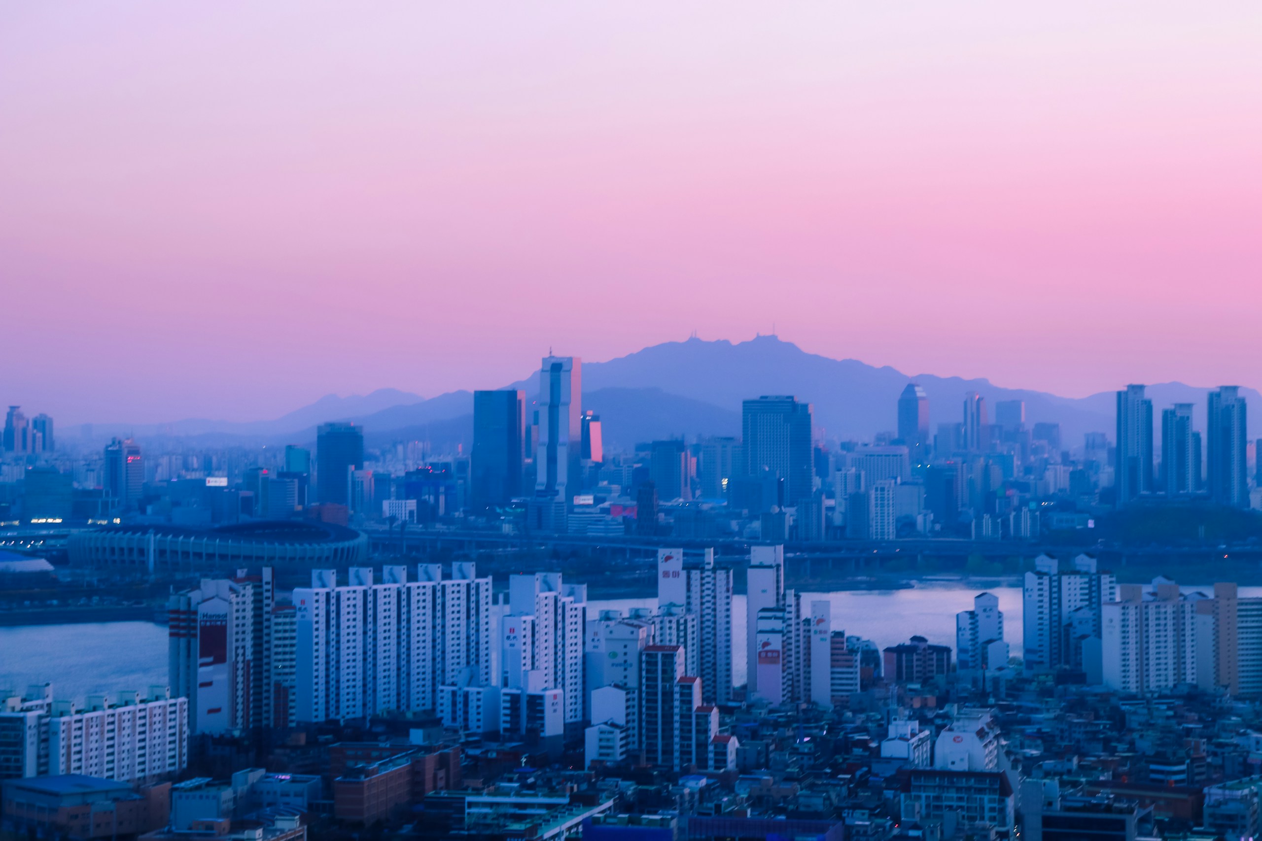 City skyline with mountains under a pink sky HD Wallpaper