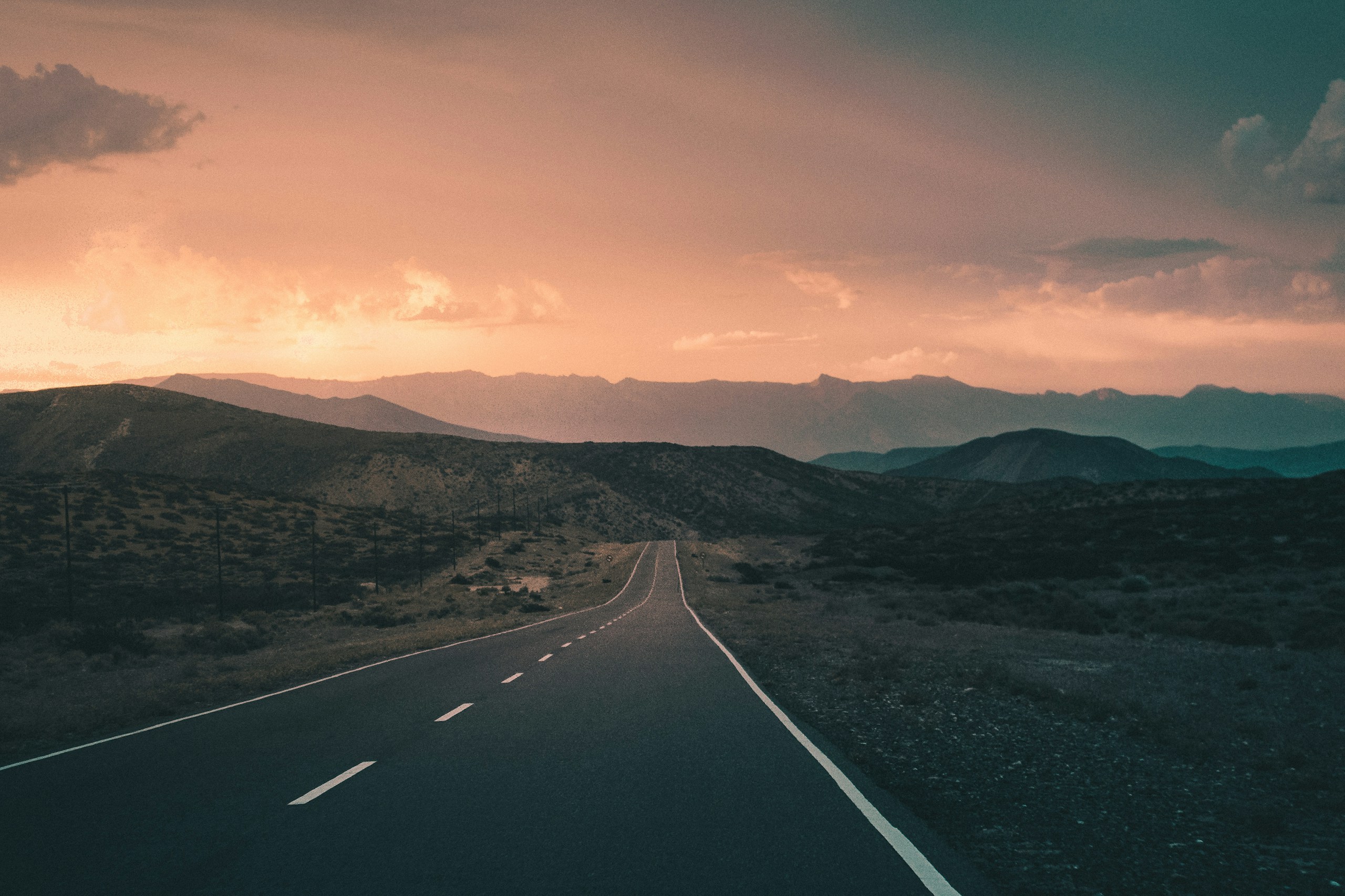 Empty asphalt road leading towards distant mountains at sunset HD Wallpaper