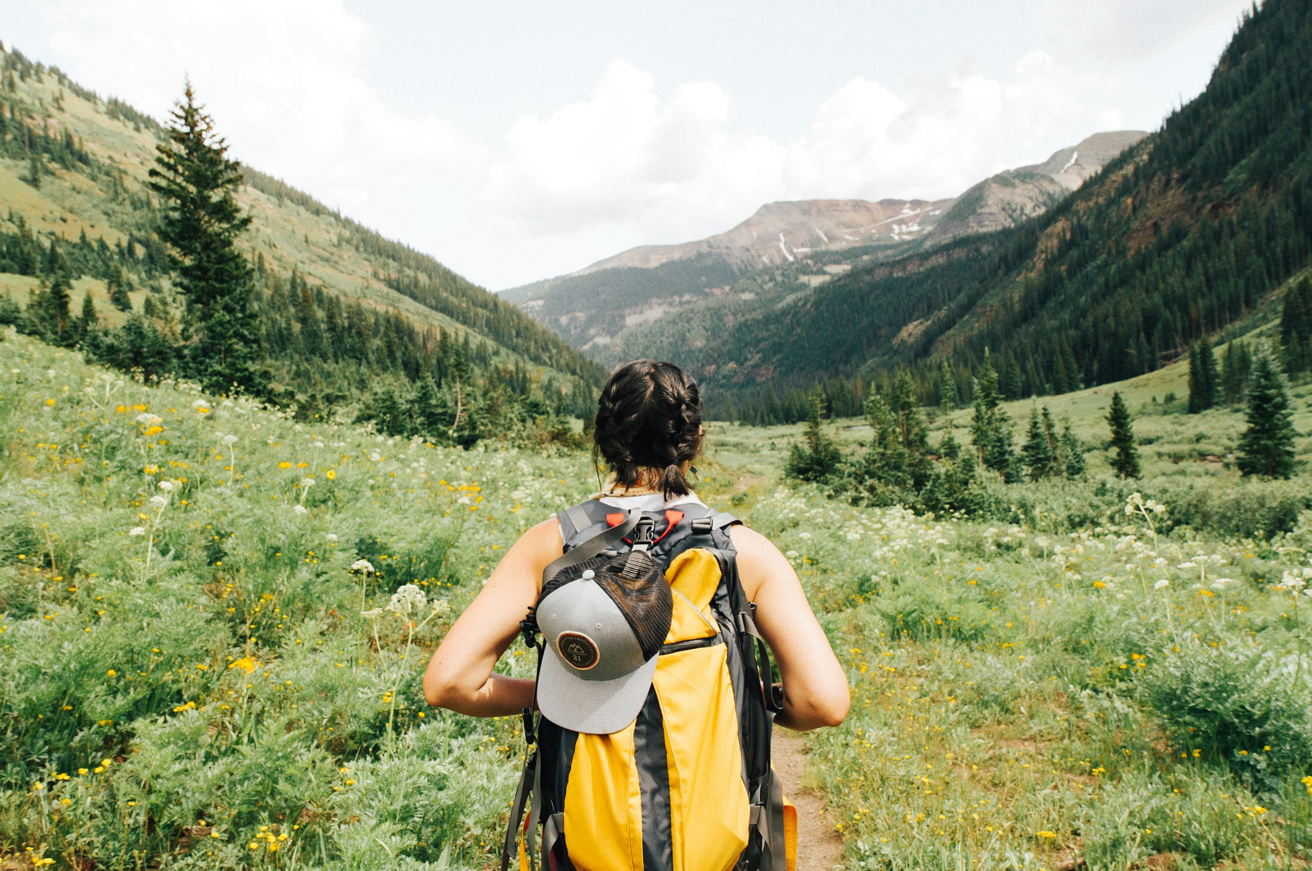 Woman hiking through a green mountain valley HD Wallpaper