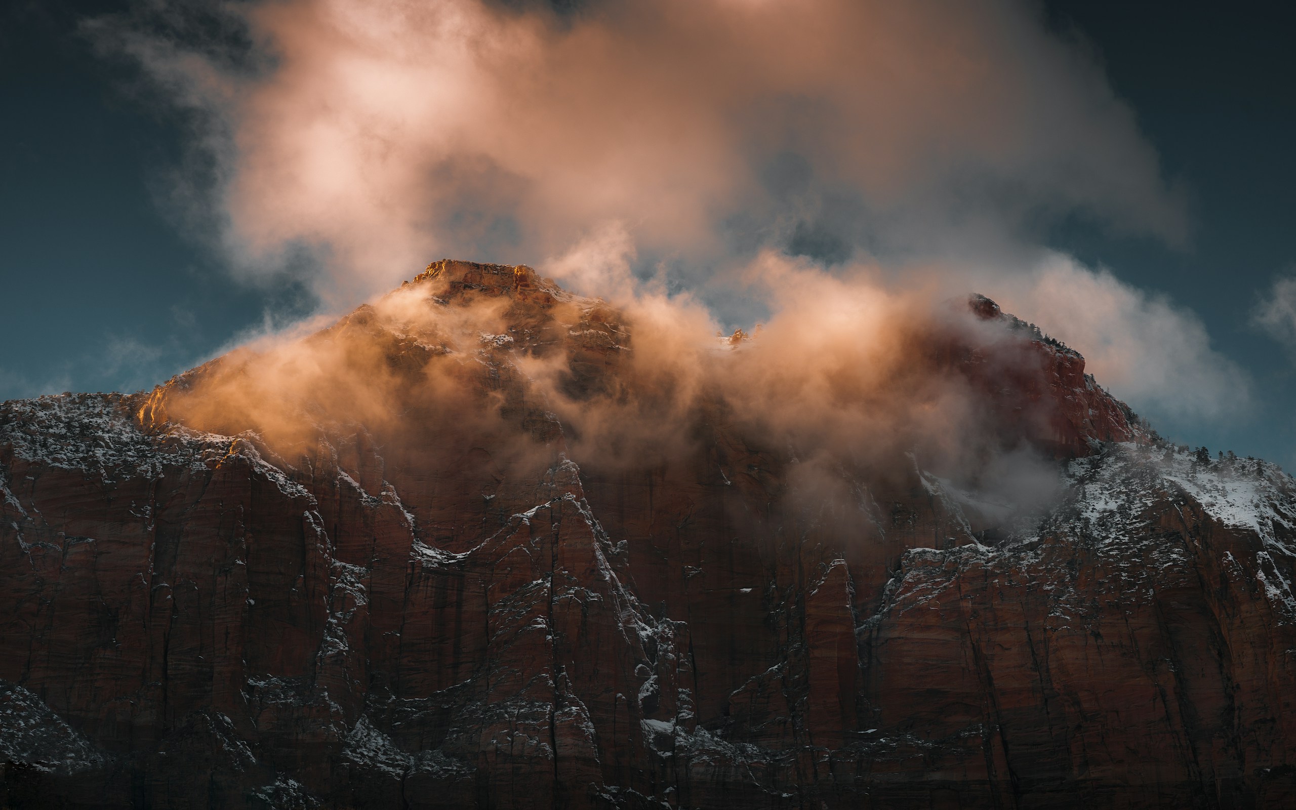 Snow-dusted red rock mountain peak shrouded in golden clouds HD Wallpaper