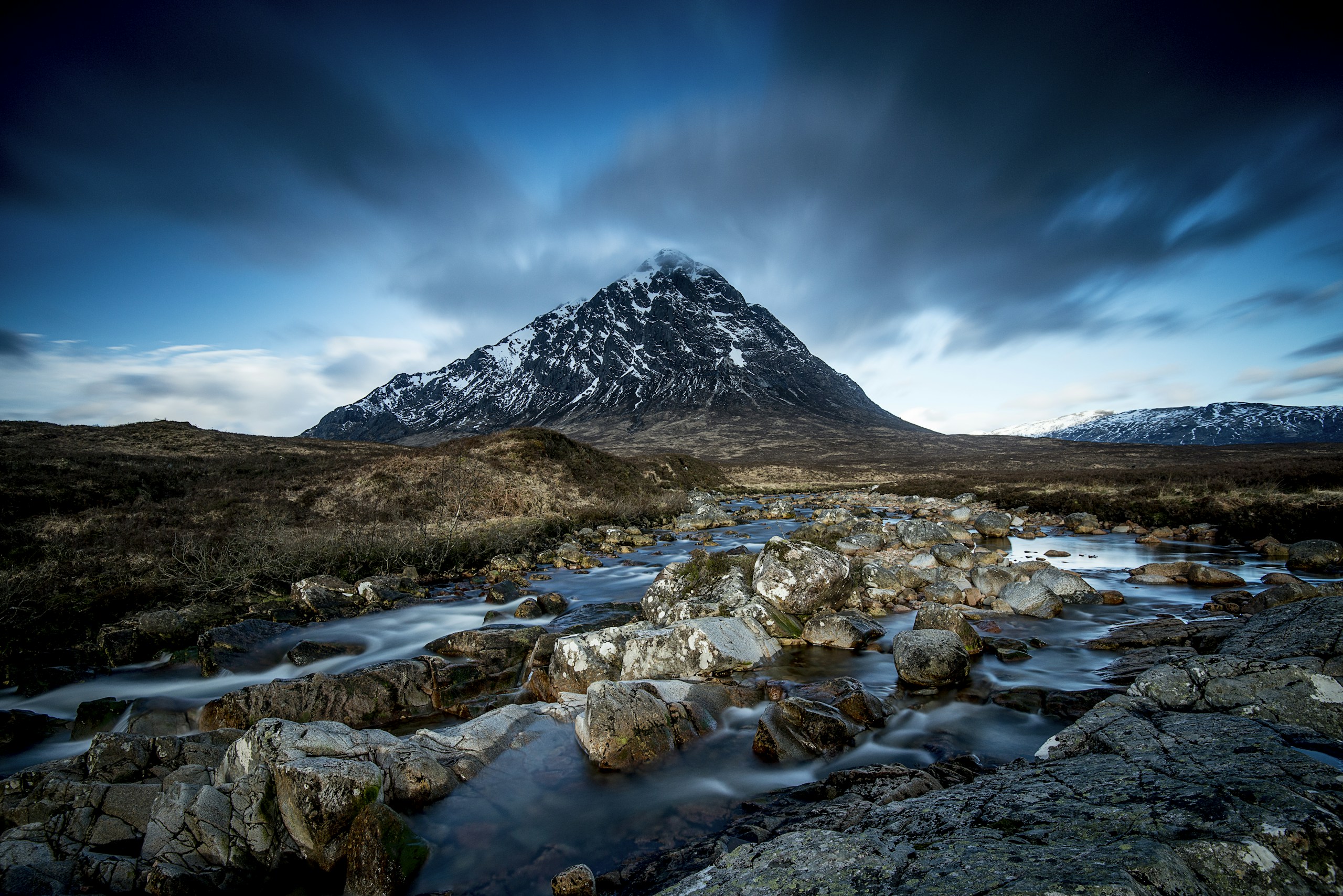 Rocky river flowing in front of a snow-dusted mountain HD Wallpaper