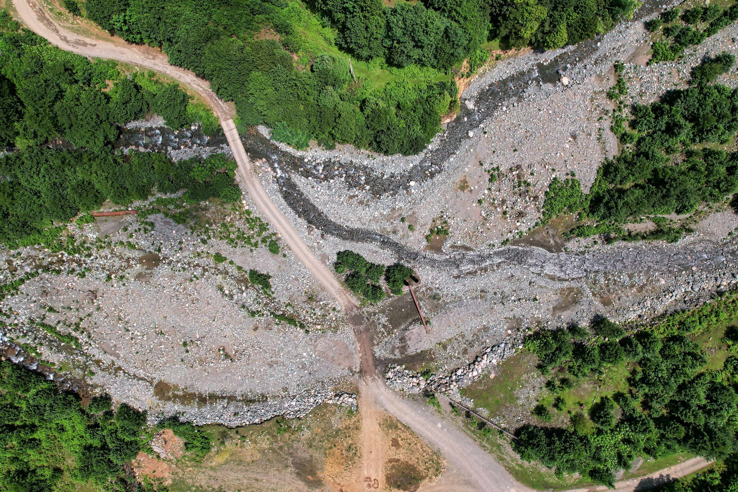 Aerial view of a dirt road crossing a rocky riverbed HD Wallpaper