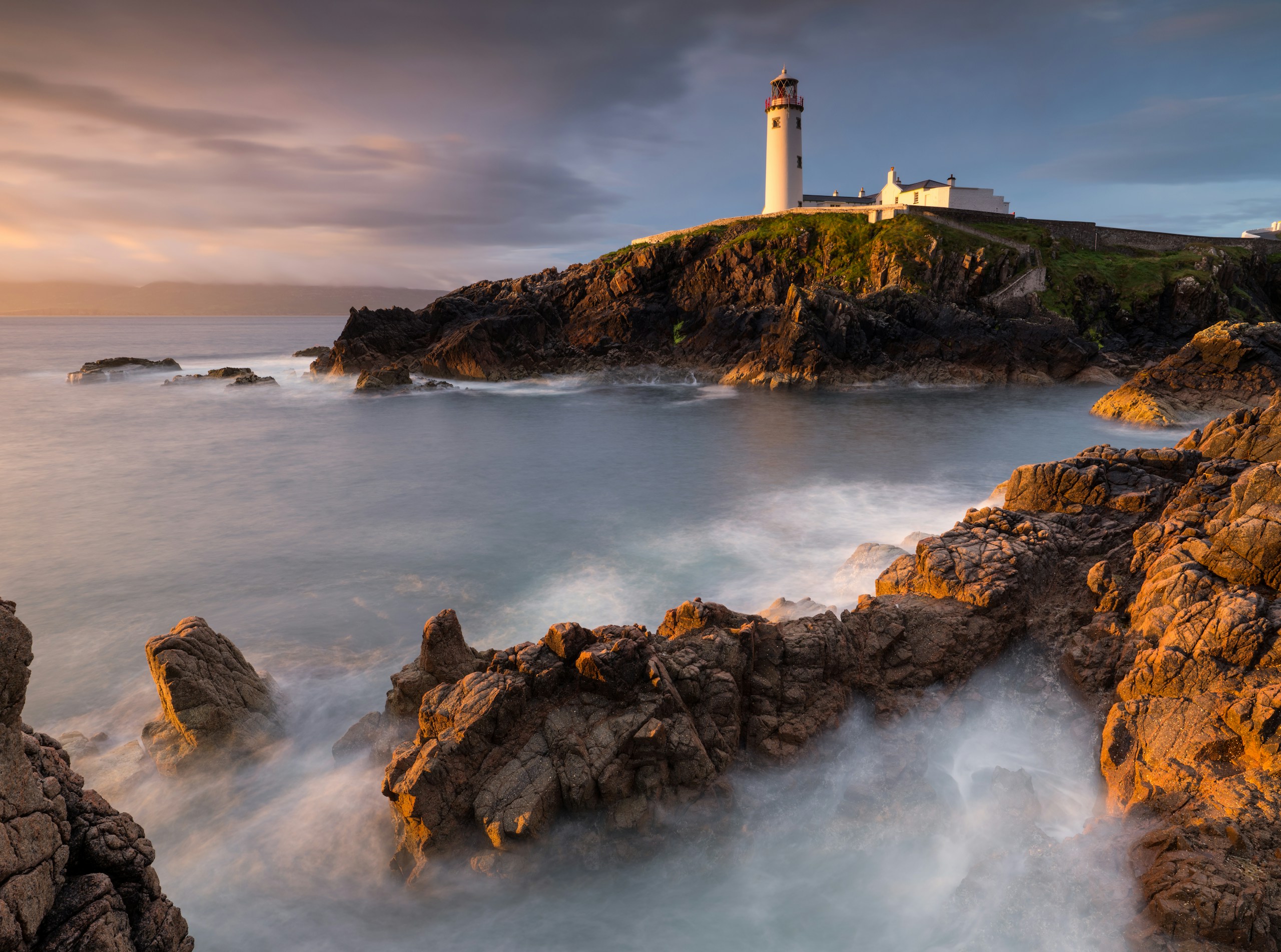 Fanad Head Lighthouse on a rocky coast at sunset HD Wallpaper