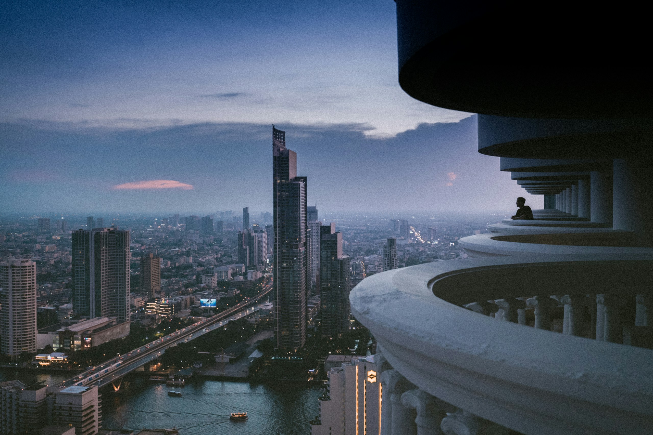 Man on high-rise balcony overlooking Bangkok cityscape at dusk HD Wallpaper