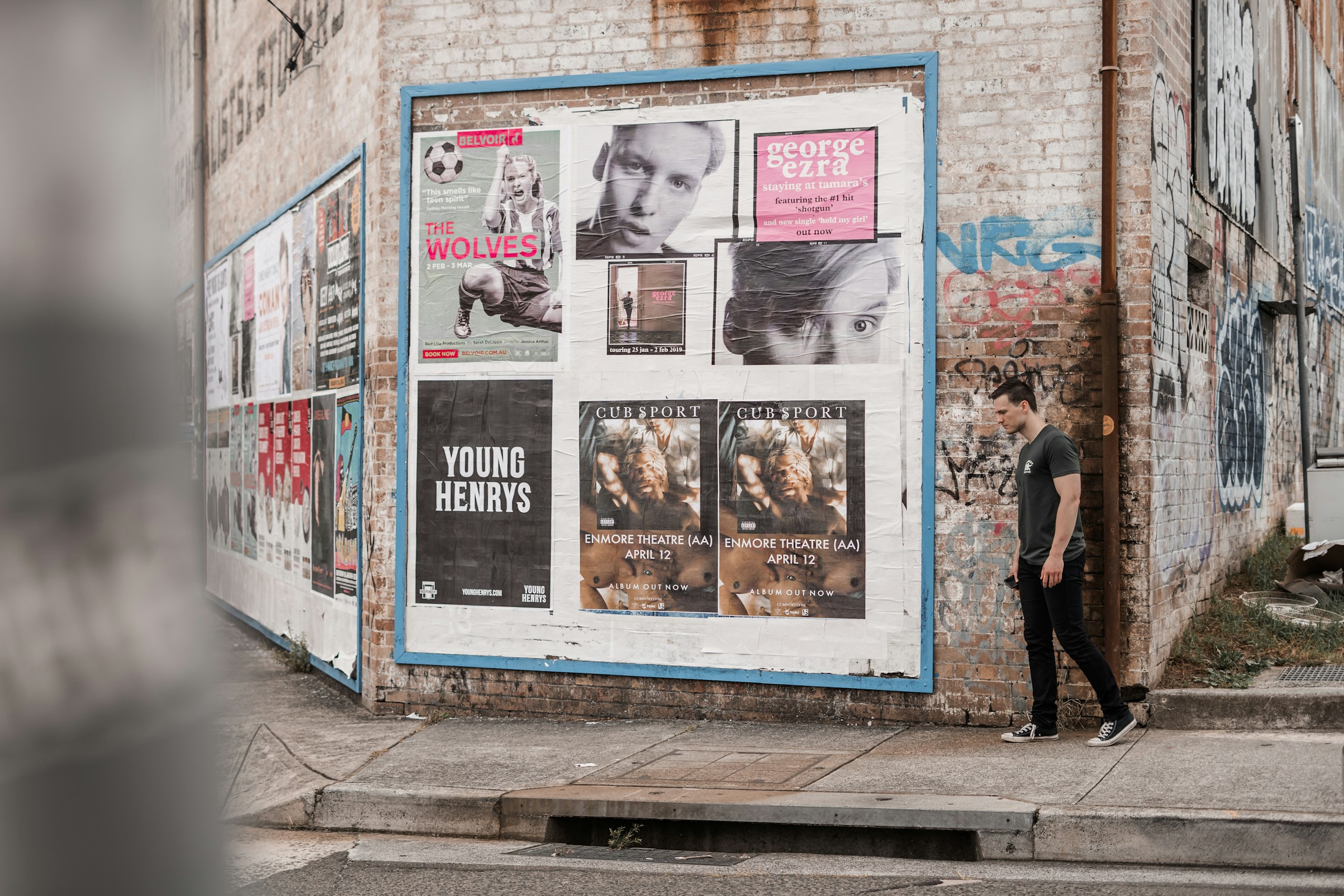 Man walking past poster-covered brick wall HD Wallpaper
