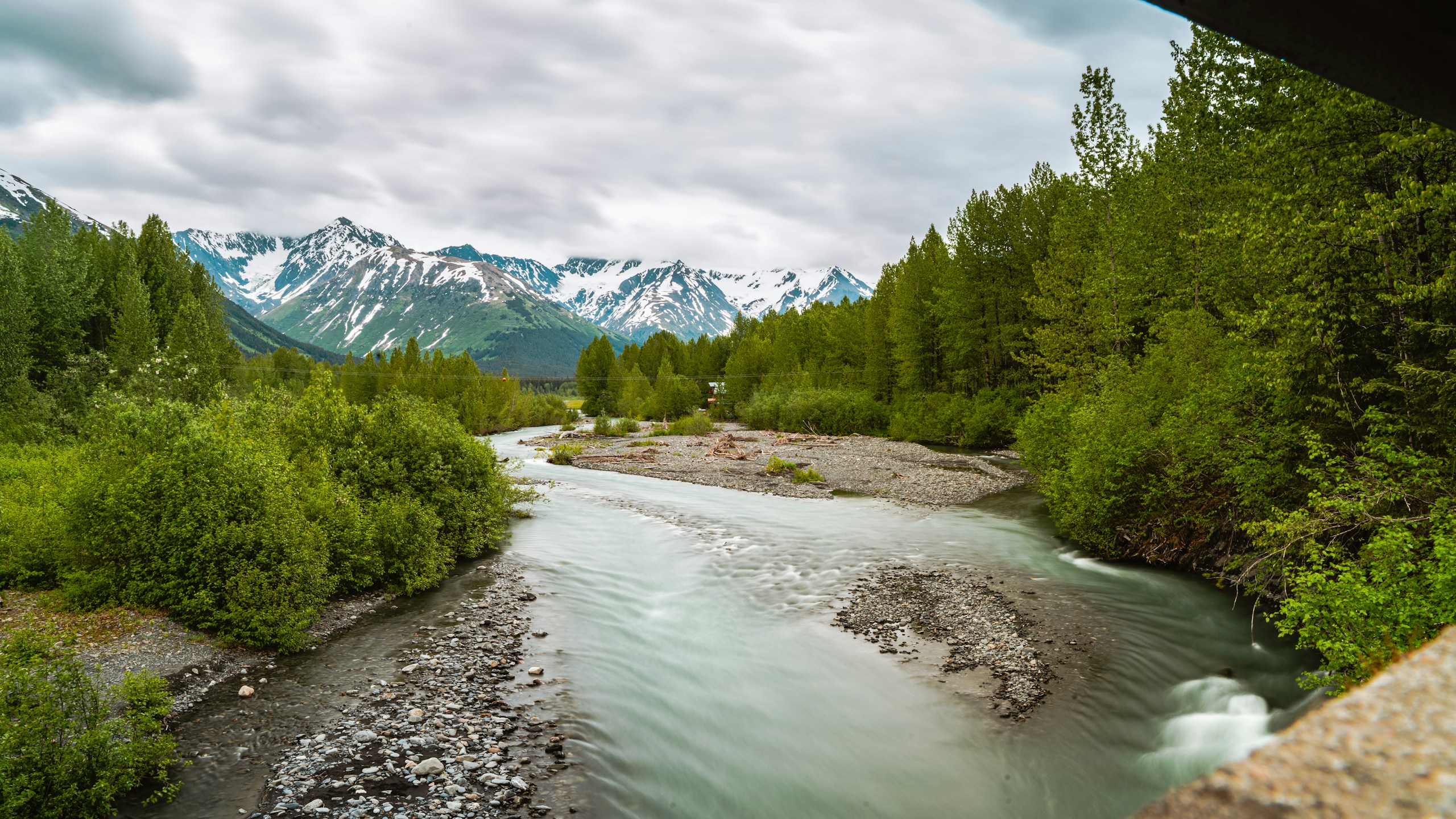 Glacial river flowing through a forested valley in Alaska HD Wallpaper