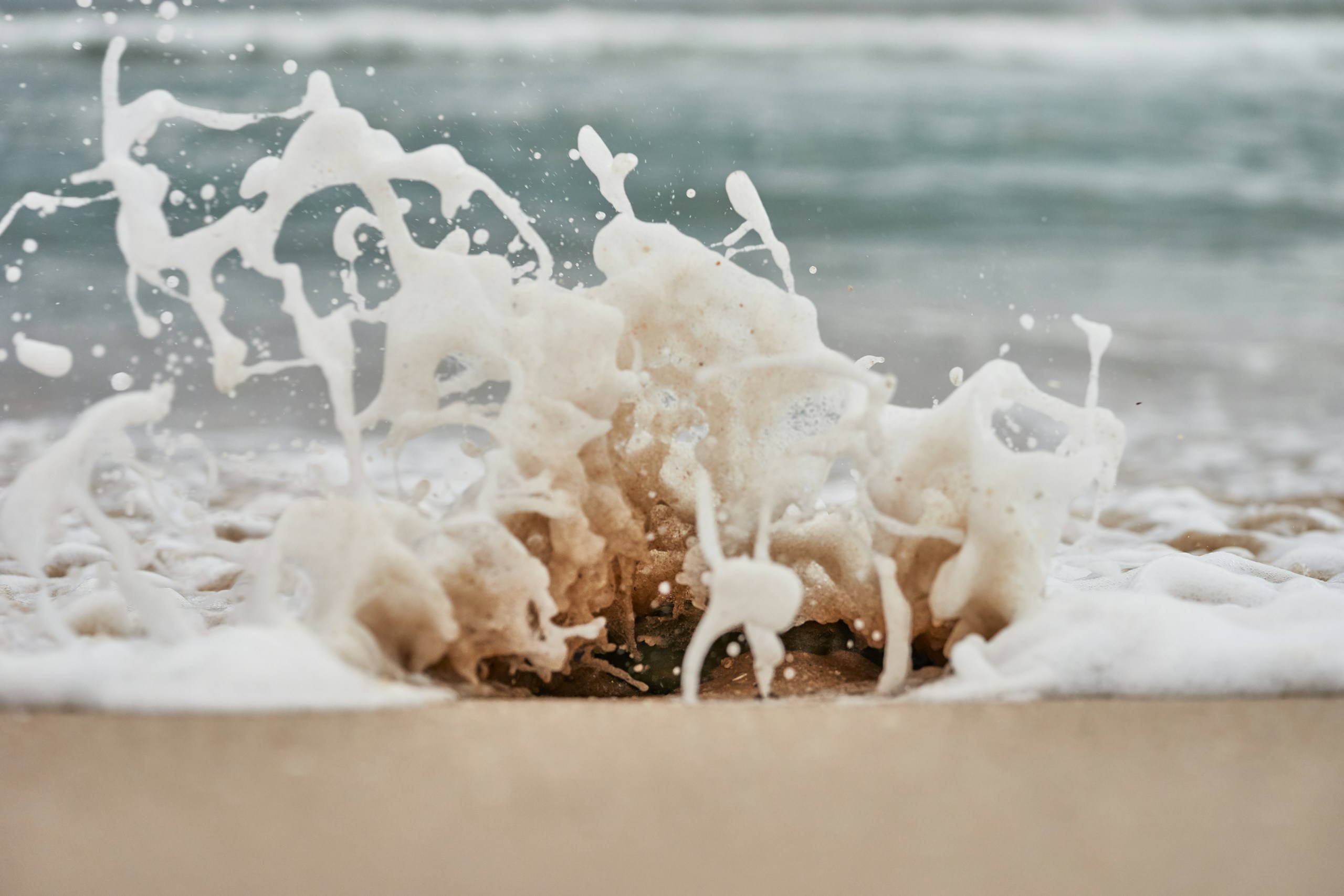 Close-up of sea foam splashing on sandy beach HD Wallpaper