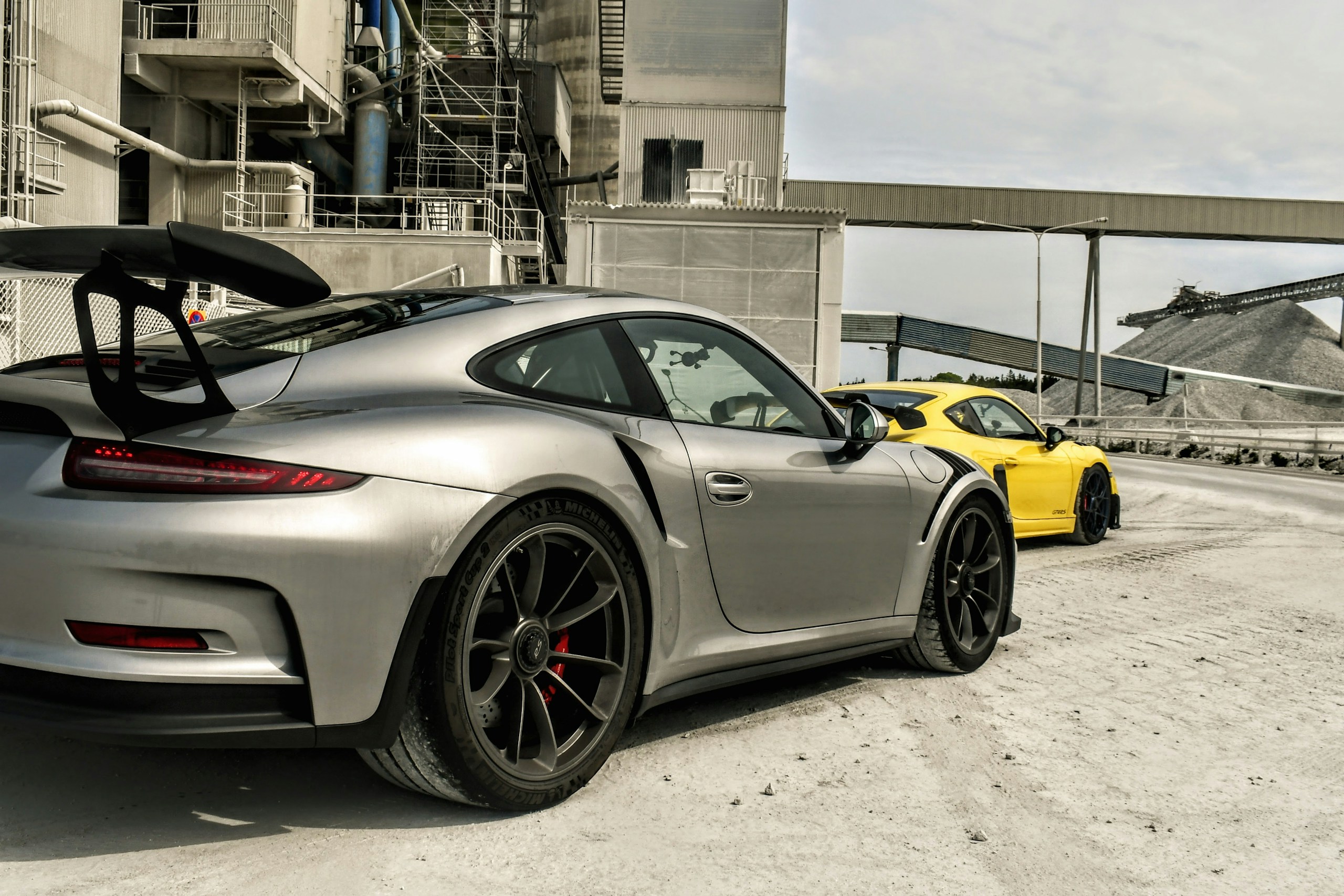 Silver and Yellow Porsche Sports Cars at Industrial Site HD Wallpaper