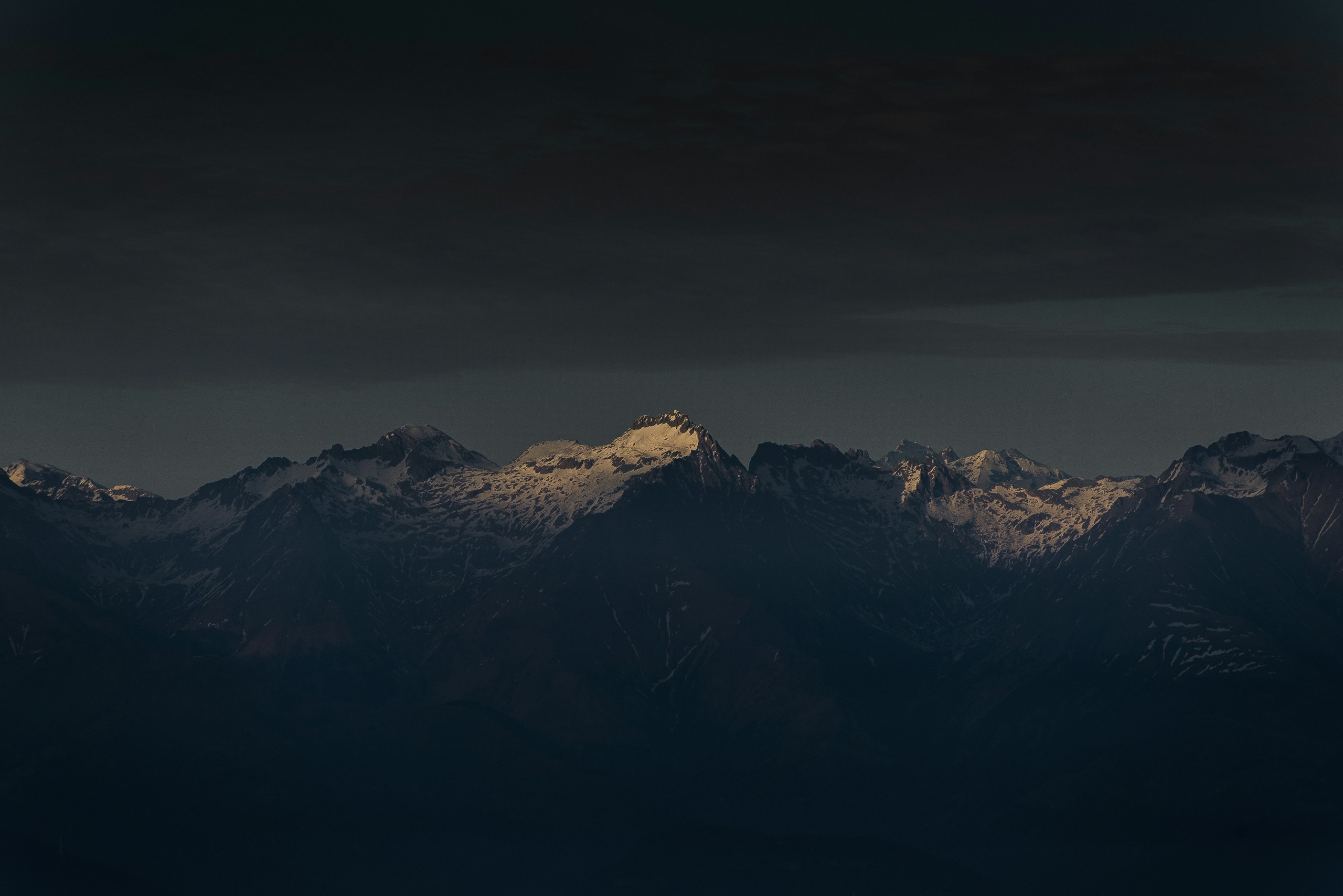 Snow covered mountain range under dark sky HD Wallpaper