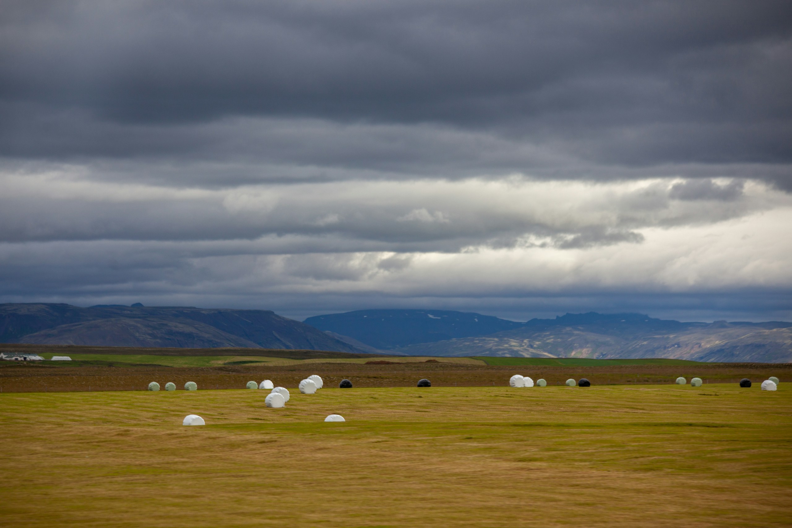 Wrapped hay bales in a field under dramatic clouds HD Wallpaper