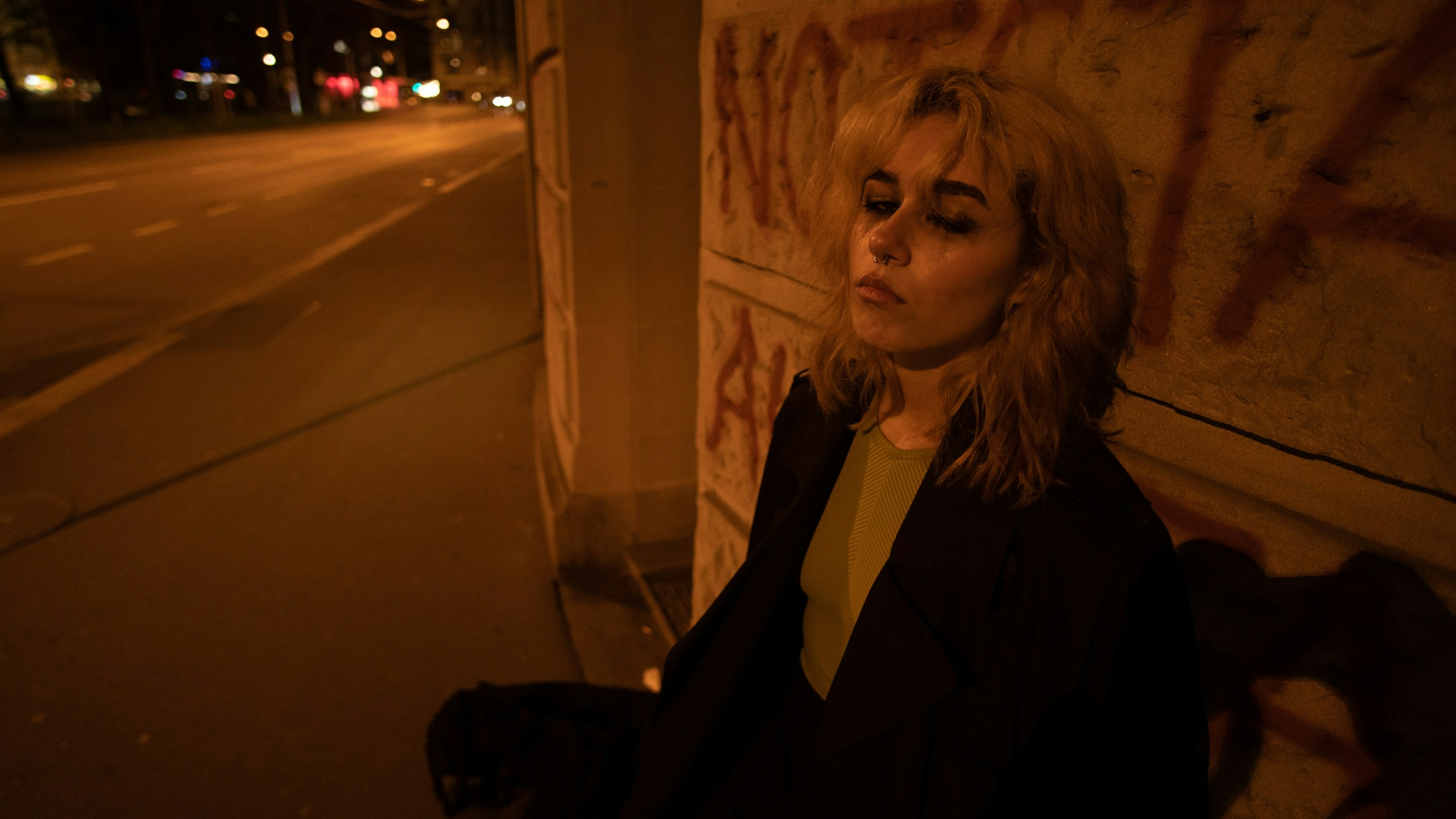 Blonde woman leaning against a graffiti wall at night HD Wallpaper