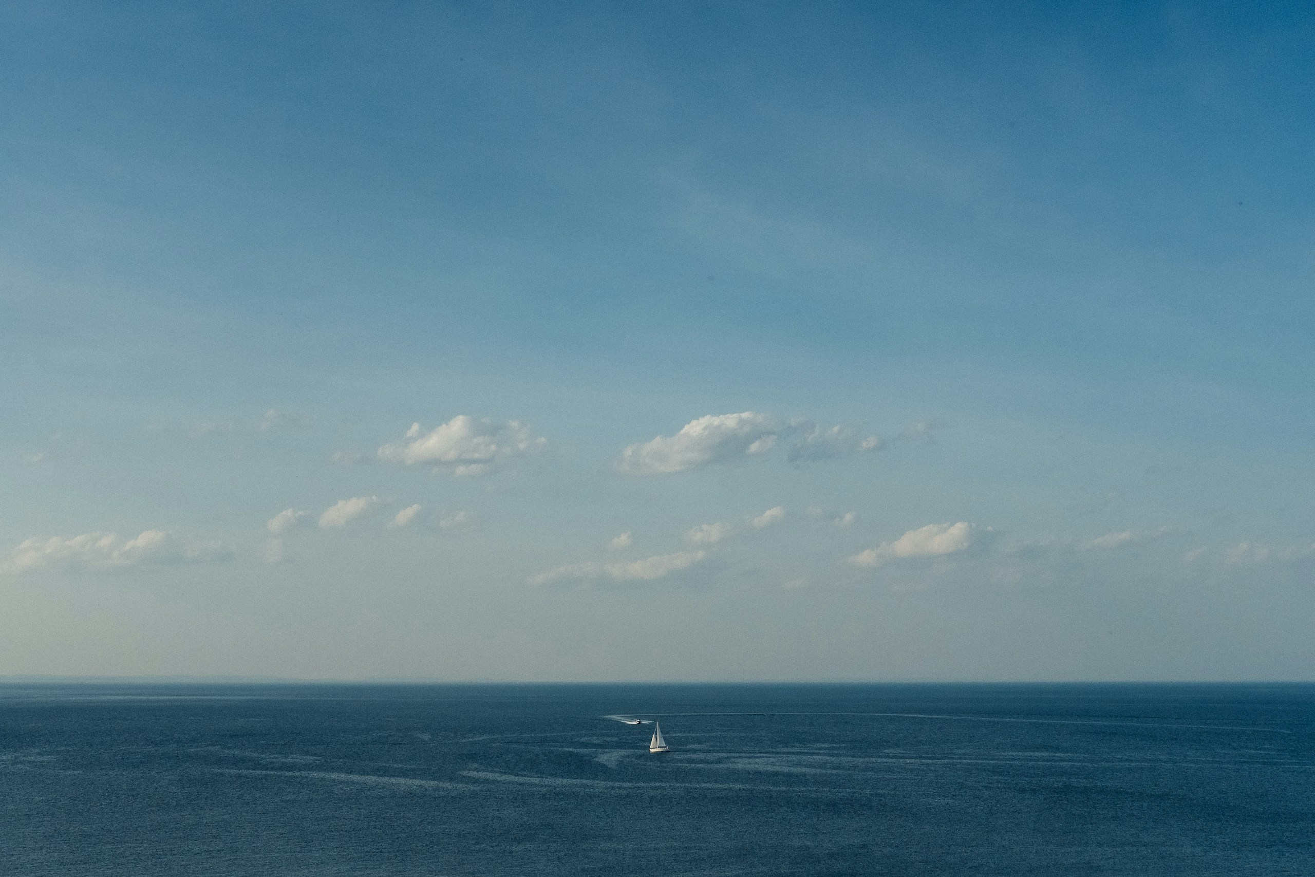 A single white sailboat on a vast blue sea HD Wallpaper