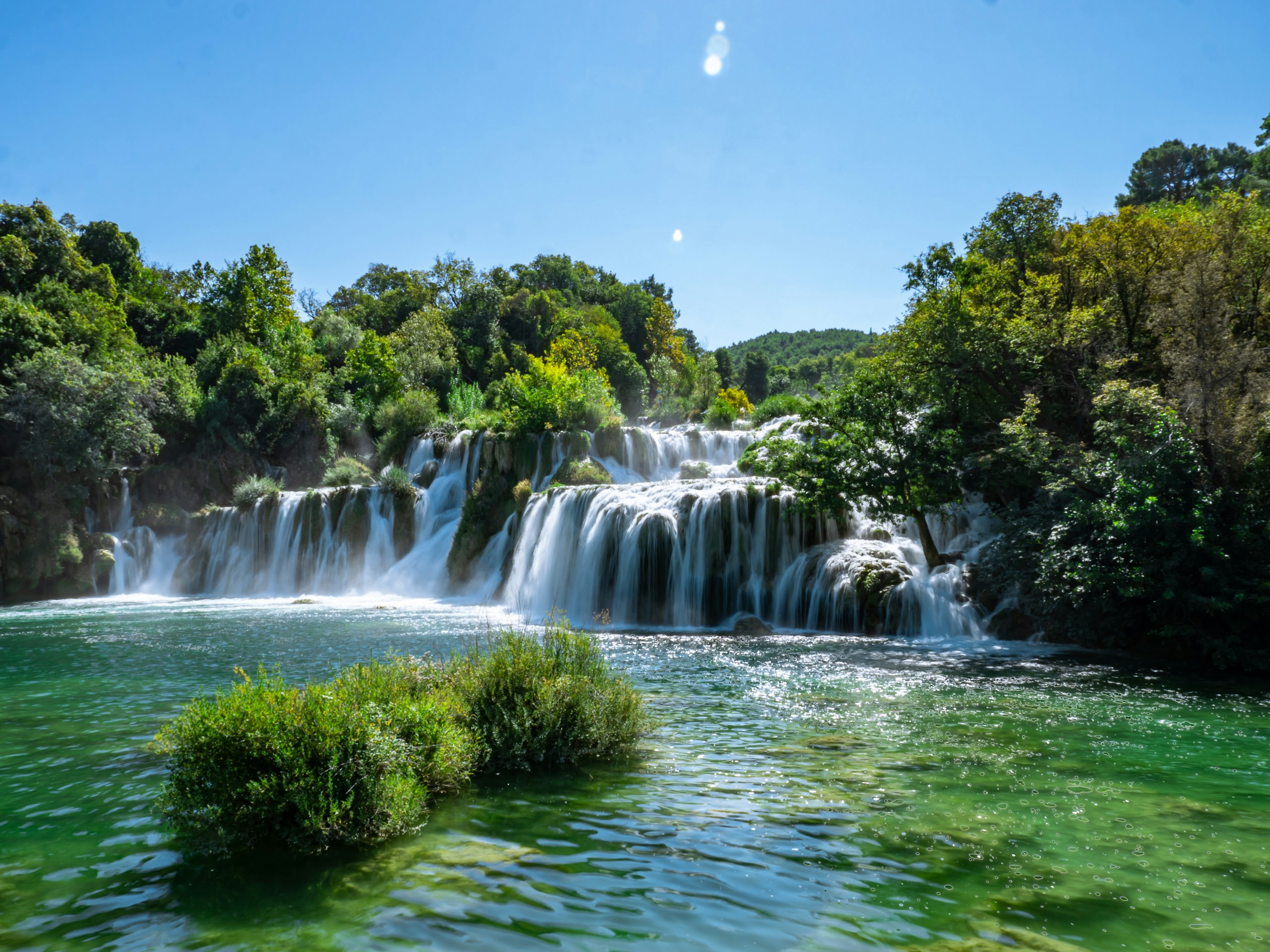 Cascading waterfall flowing into a clear green pool HD Wallpaper