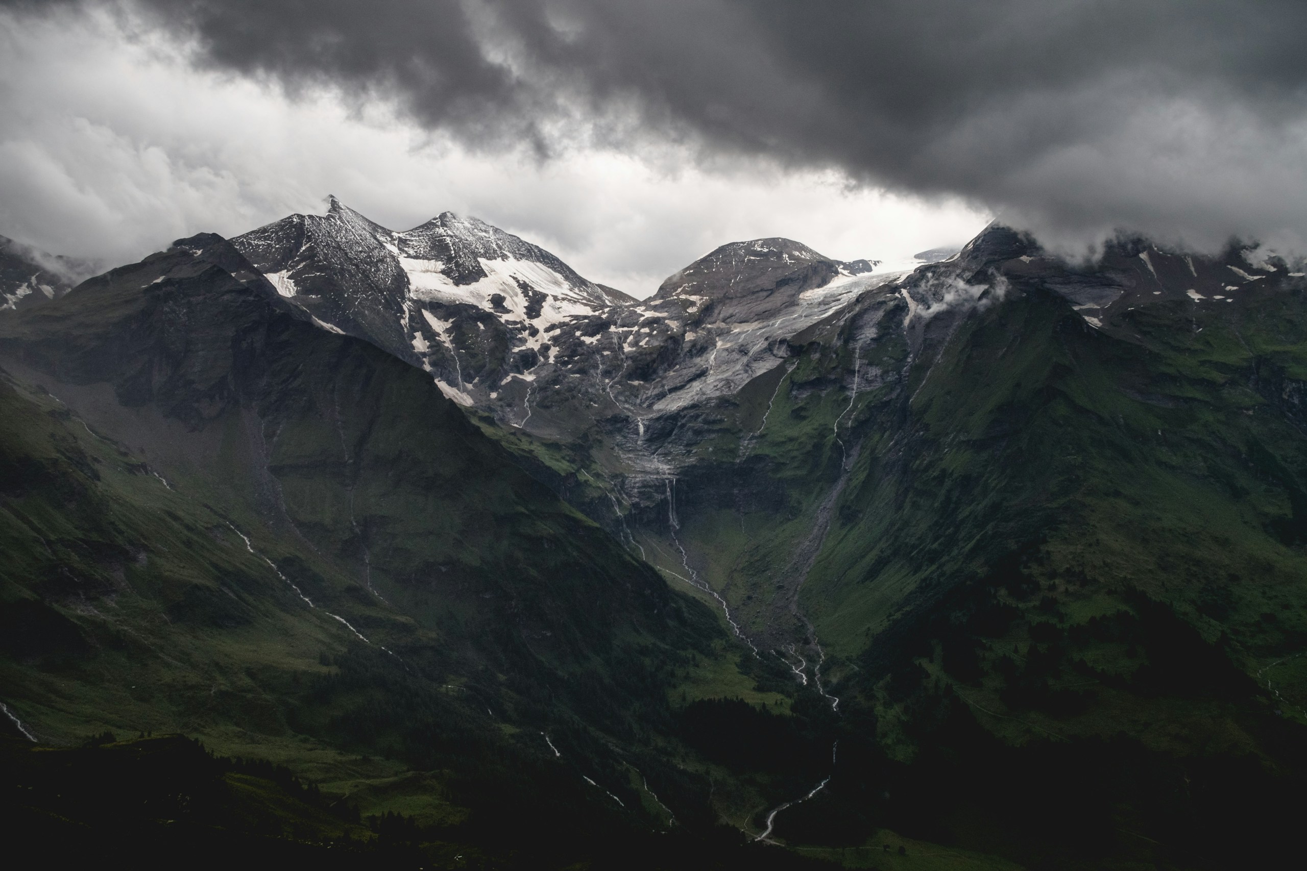 Snow-capped mountain peaks under dark storm clouds HD Wallpaper