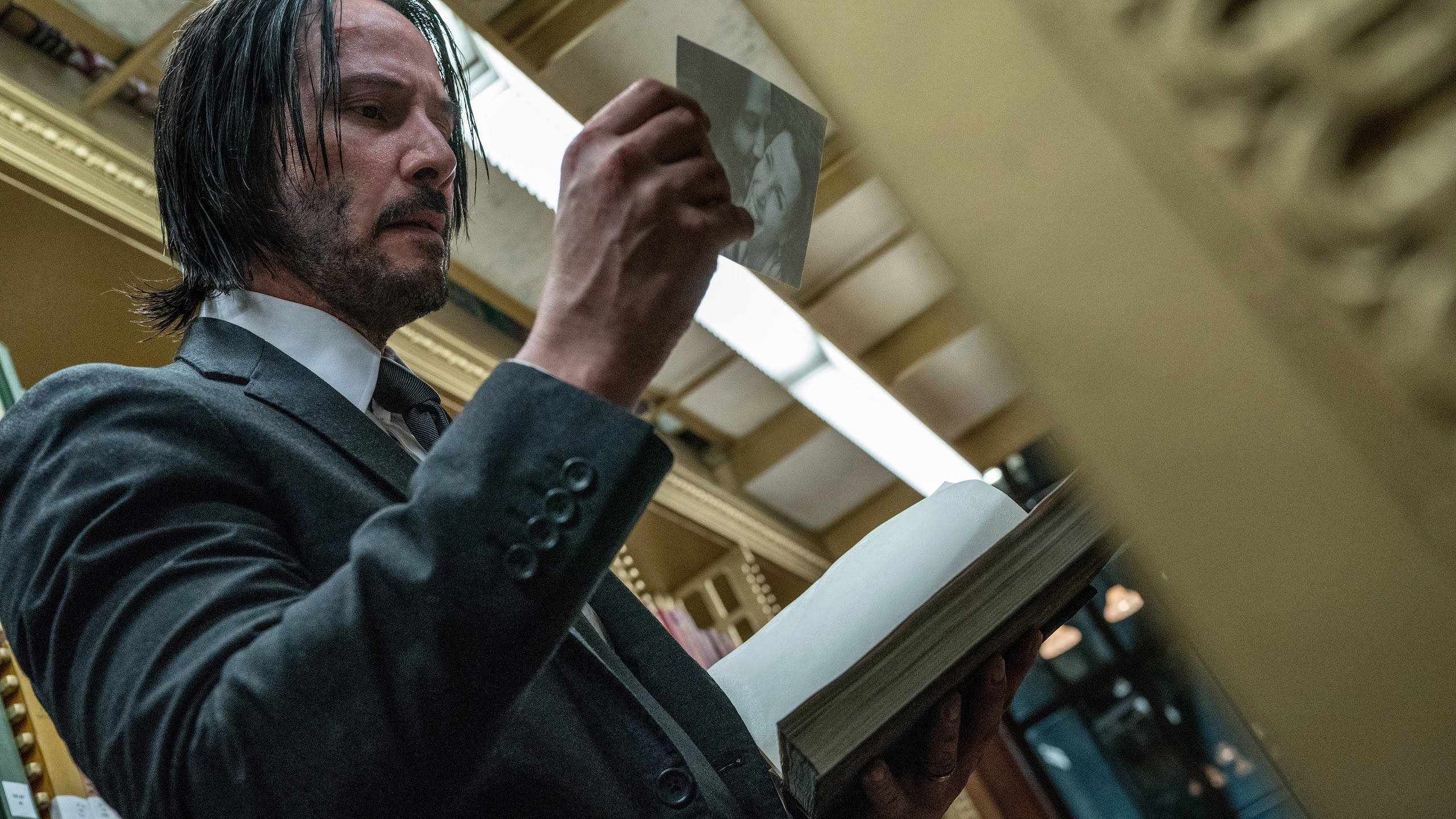 John Wick holding a photograph in a library HD Wallpaper