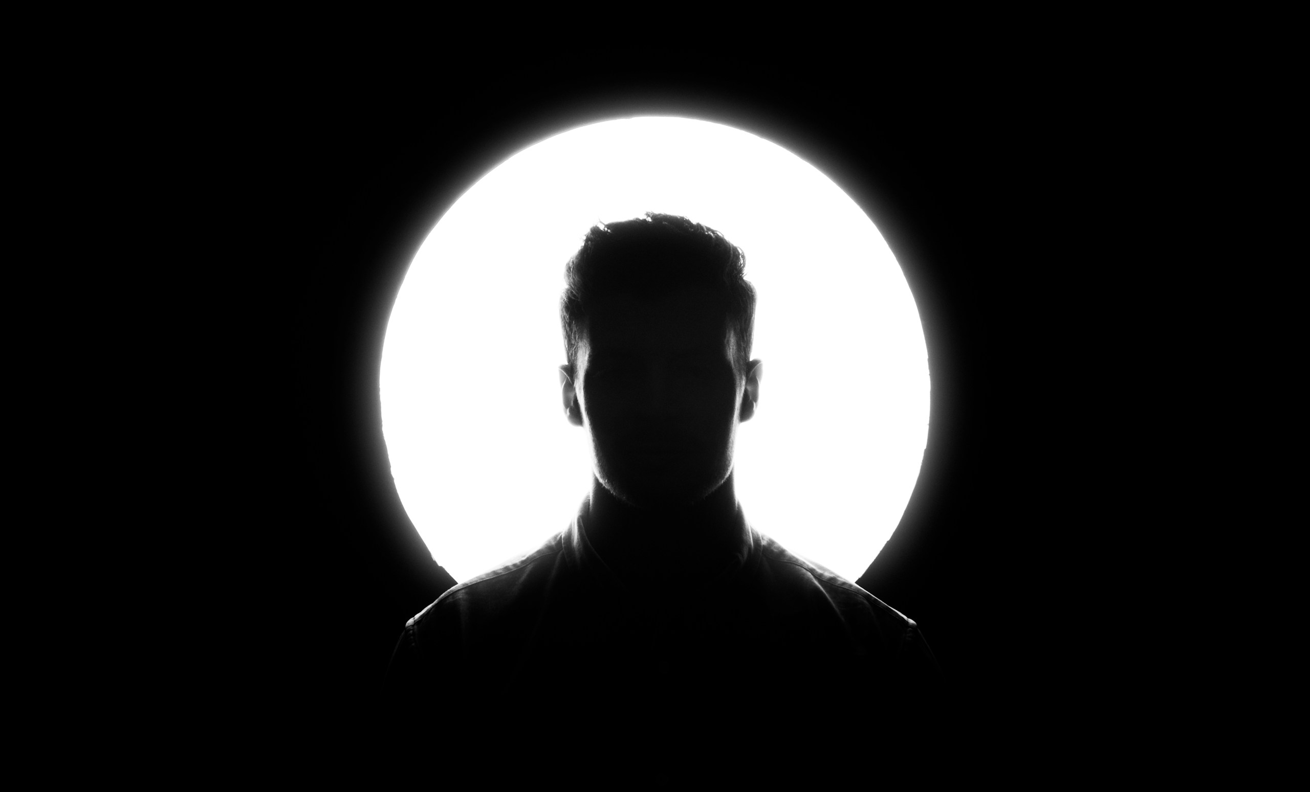 Silhouette of a man against a bright circular light HD Wallpaper